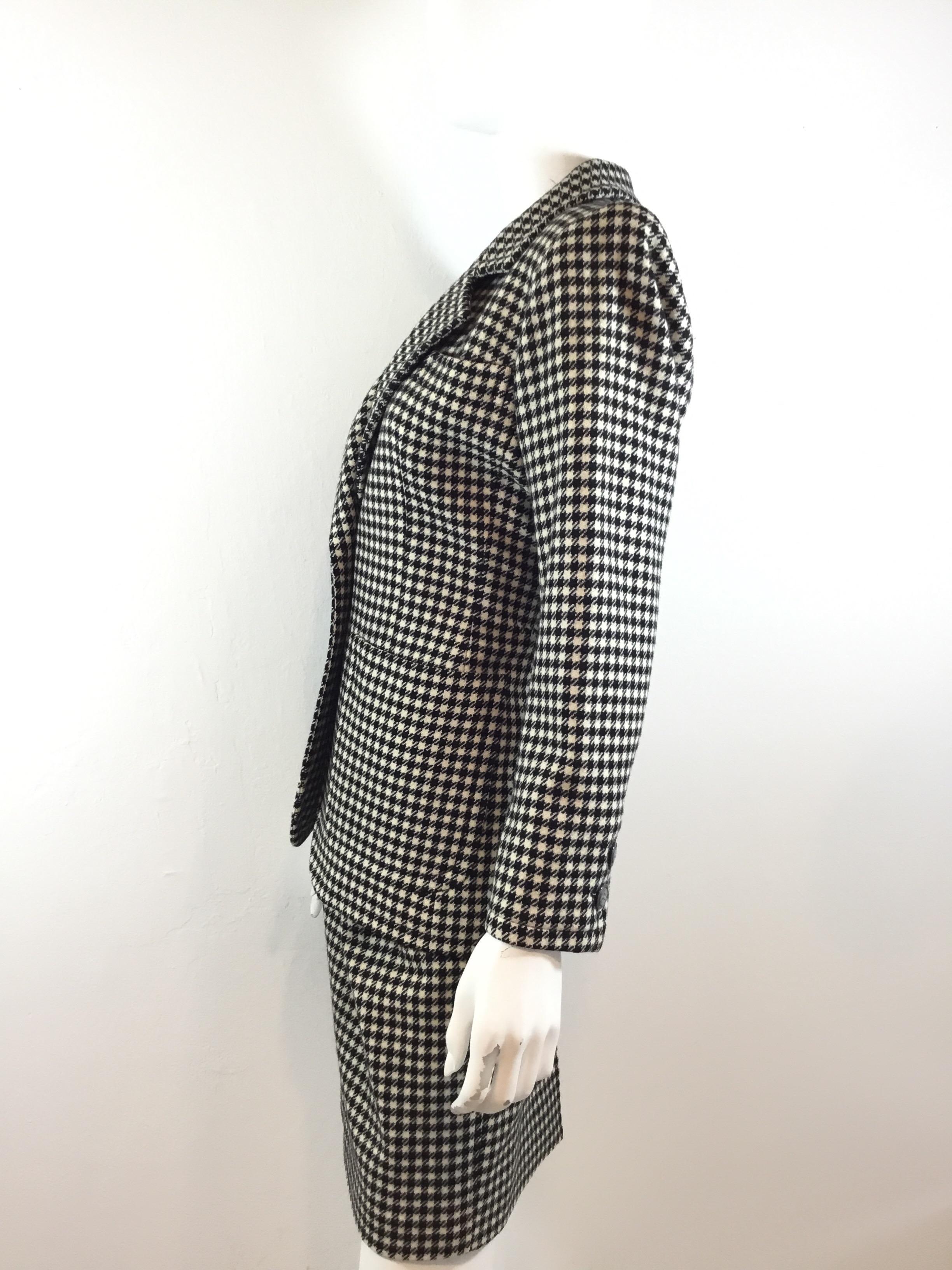 Vintage Yves Saint Laurent skirt suit featuring a Cream and black houndstooth pattern throughout. Jacket has button closures along the front and on the cuffs, and two slip pockets at the hem. Skirt has pockets at the hips and a sid zipper fastening.