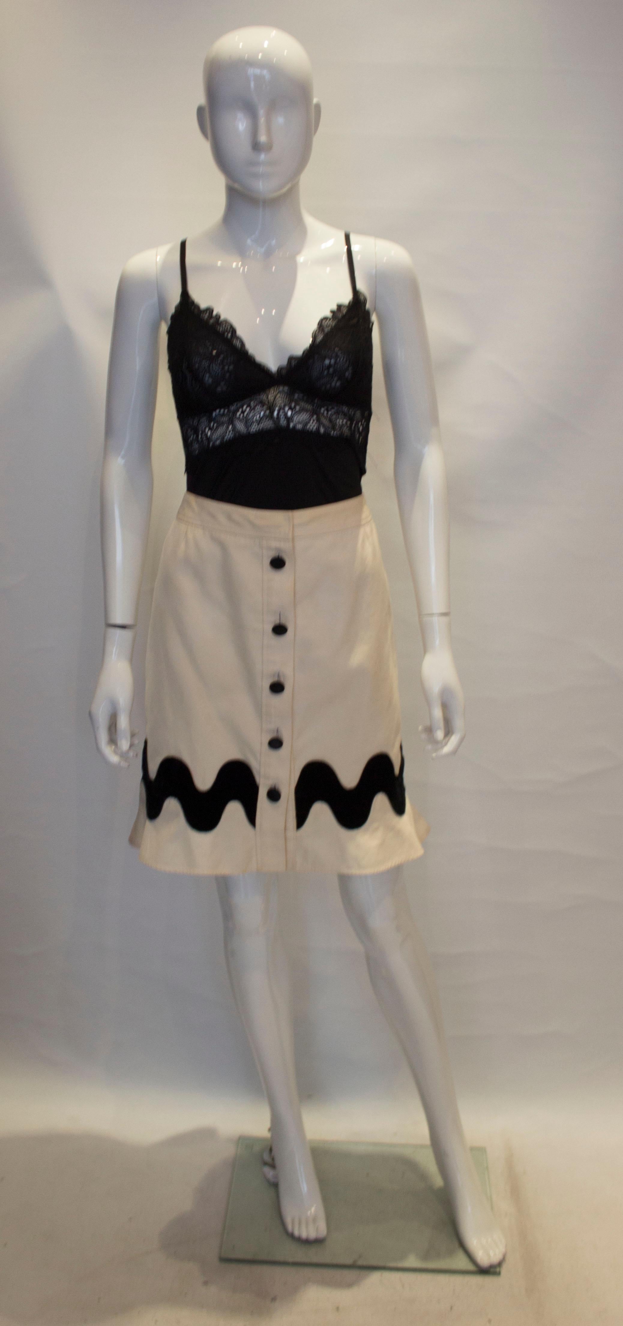 A fun skirt for Fall by Yves Saint Laurent. The skirt is in a white linen mix with a button through front and frill at the hem. It has a five button opening with velvet covered buttons, and velvet  band  near the hem. It is fully lined.