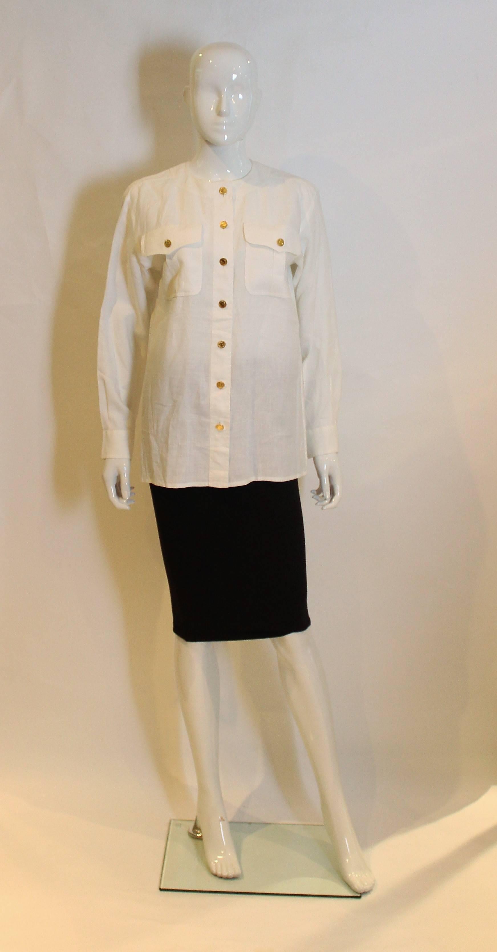 A great shirt for Spring /Summer by Yves Saint Laurent, Rive Gauche. In a white linen, this shirt has a round neckline, 2 breast pockets with gold buttons, a seven button opening at the front and a button on each cuff.