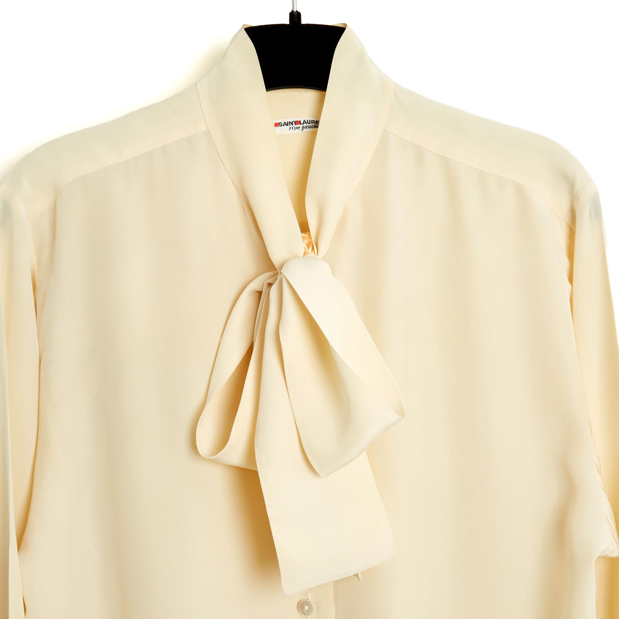 Camicetta Yves Saint Laurent Rive Gauche circa 1985 in crepe di seta ecru, taglio dritto, colletto a fiocco chiuso da 6 bottoni in madreperla, maniche lunghe (larghe) chiuse da un bottone abbinato. Non c'è più la composizione o l'etichetta della