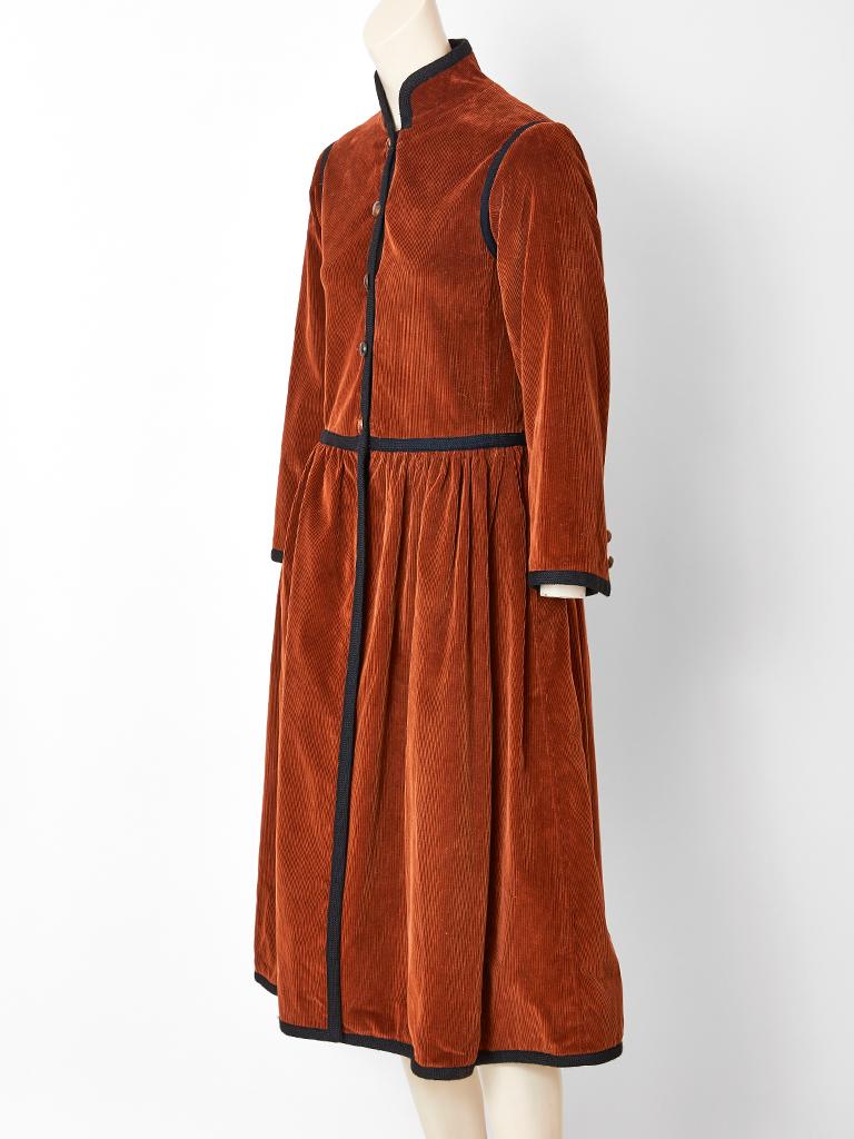 Yves Saint Laurent, Rive Gauche, rust tone, corduroy, Russian Collection, Cossack style coat, having a slightly fitted semi dropped waist bodice, and a gathered skirt. Coat has a Mandarin collar with black braid embellishment, edging the collar,