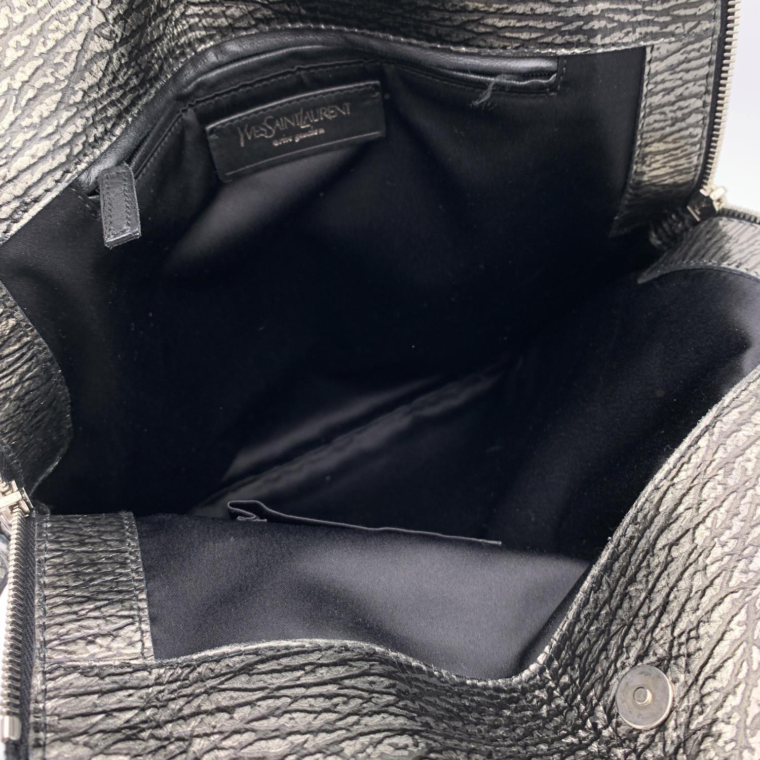 Yves Saint Laurent 'Metropolis Tribute Bag', crafted in silver tone textured leather. It features a sleek design in with side zip detailing , an ID tag and gold metal hardware. Magnetic button closure on top. Black satin lining. 1 side zip pocket