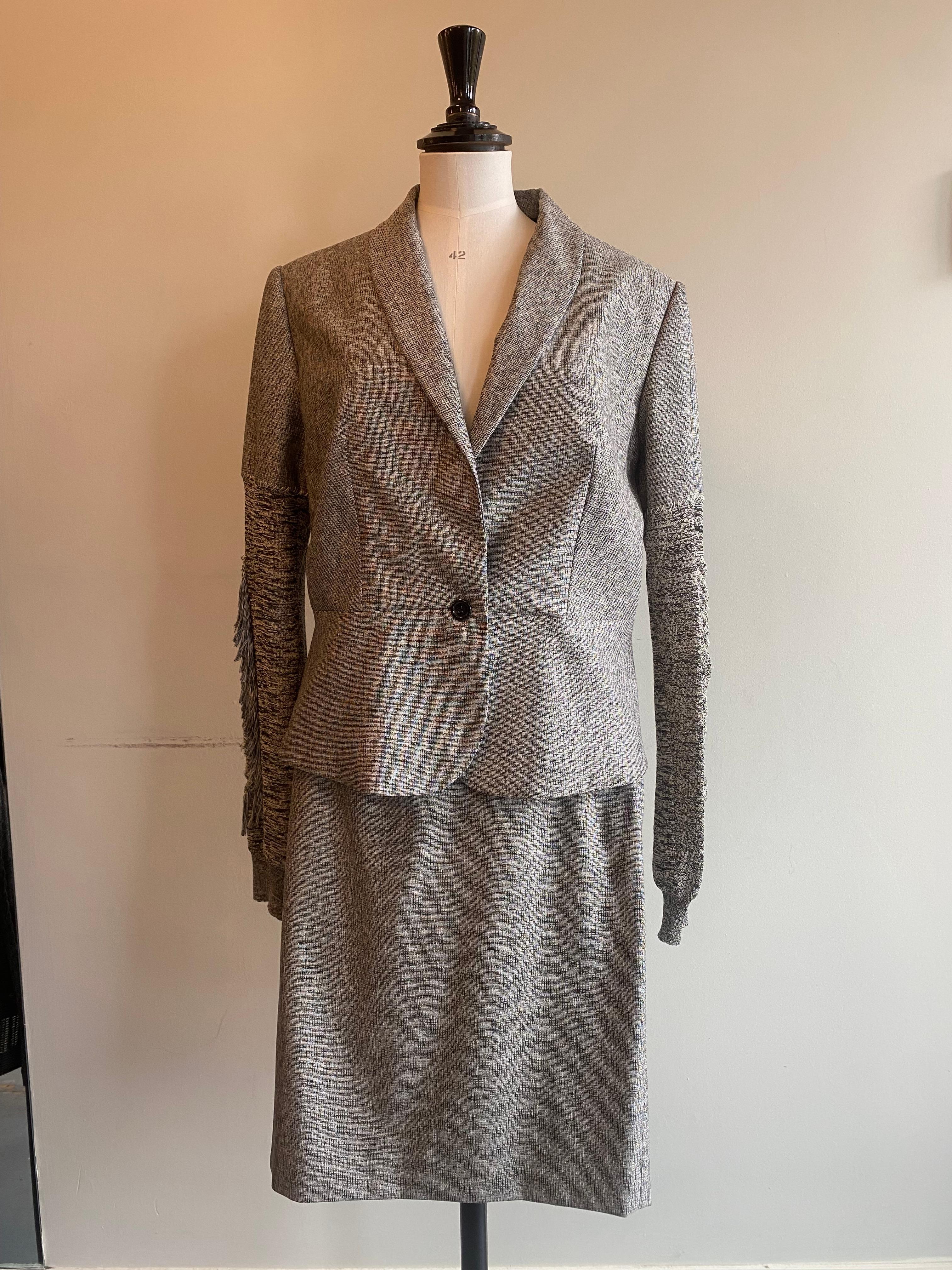 Yves Saint Laurent skirt suit from the eponymous brand. Wool/silk mix suit fastened with a single black button. Raw style stitching connects the grey textured waistline and sleeves with tassel detail. Made in France. Marked size F44. Fabric content: