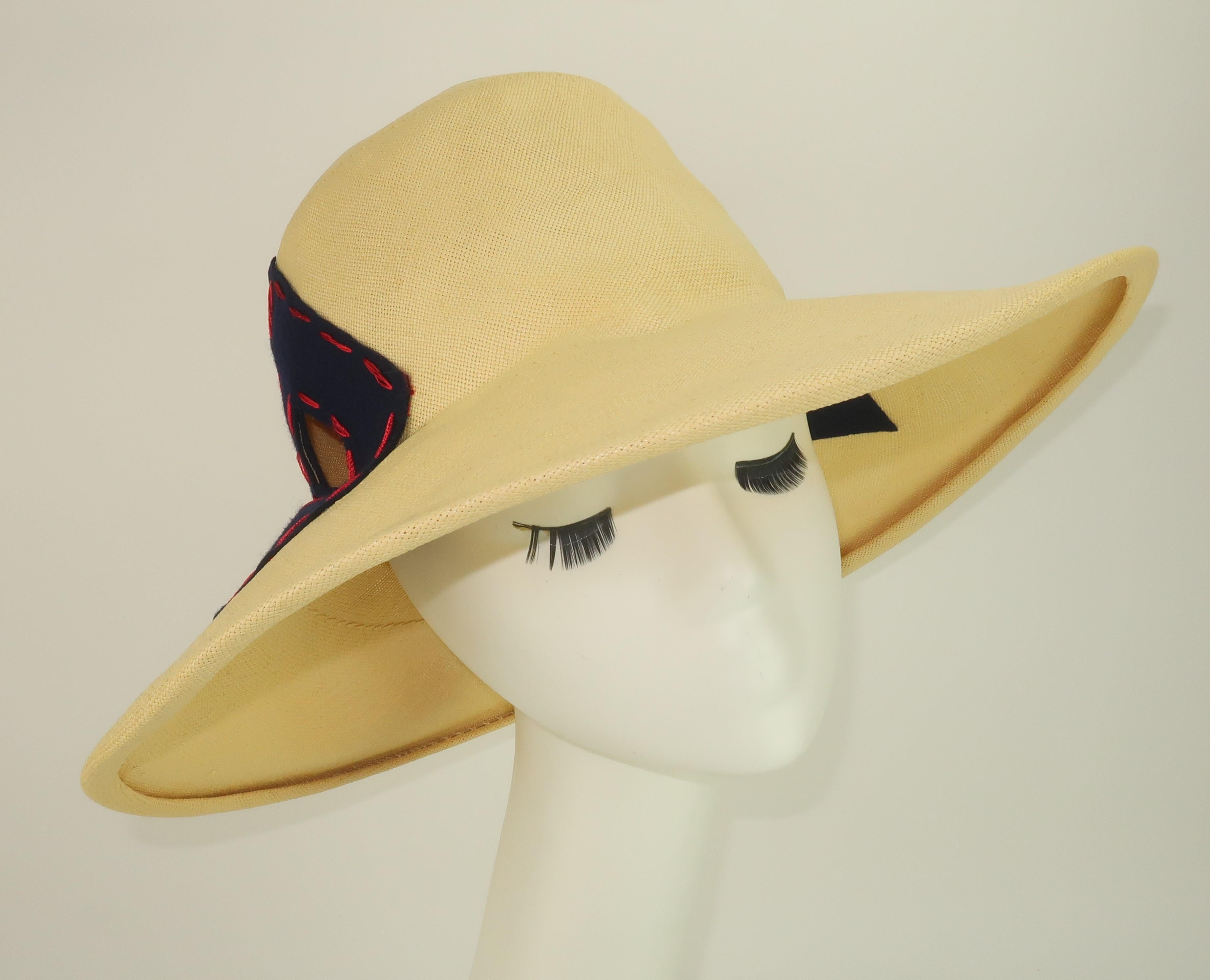 1970's Yves Saint Laurent natural straw hat with two diamond shaped cut outs framed in dark navy blue felt stitched in contrasting red.  The diamond shapes are replicated on the inside of the hat, as well.  The straw is beautifully woven and