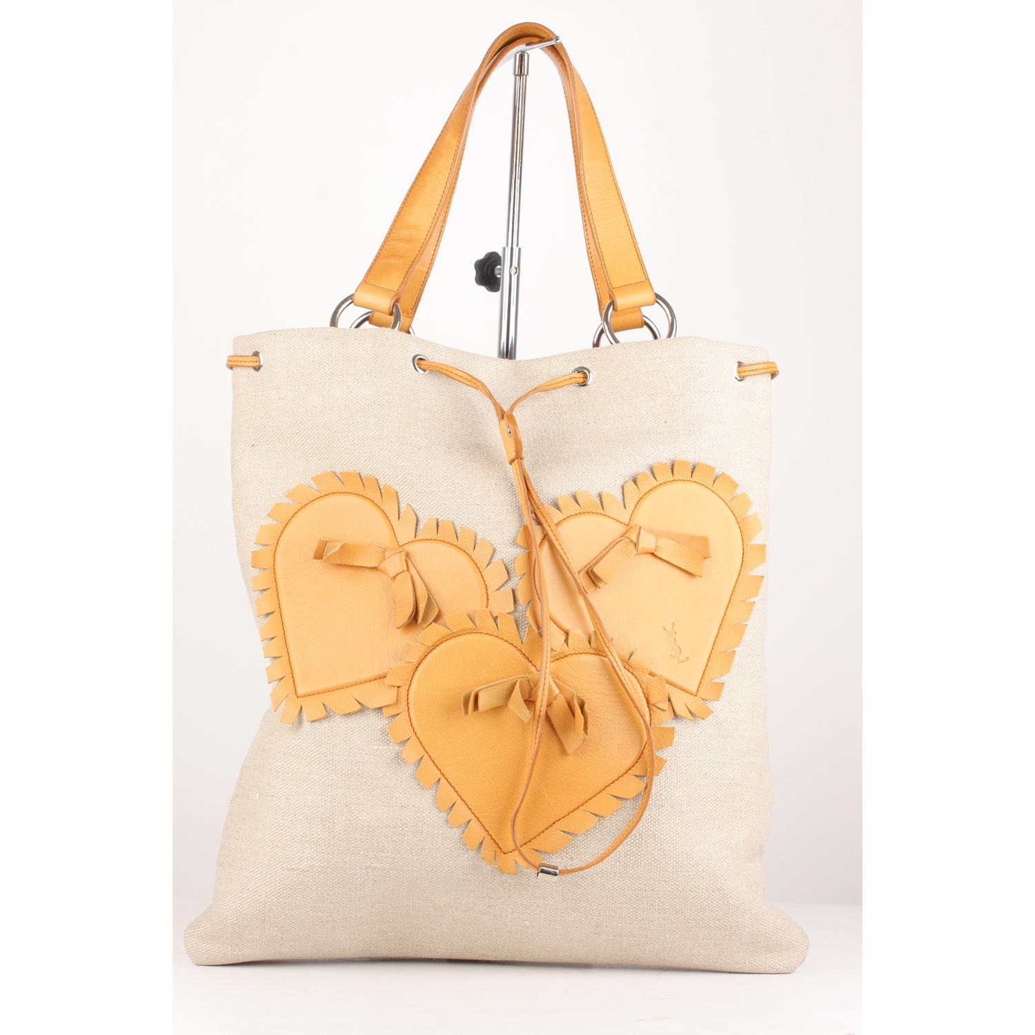 YVES SAINT LAURENT tan canvas tote bag decorated with three lovely hearts on the front. Drawstring closure on top. Double leather handles/straps. Orange satin lining. 1 side zip pocket inside. 'YVES SAINT LAURENT Rive Gauche' embossed inside.