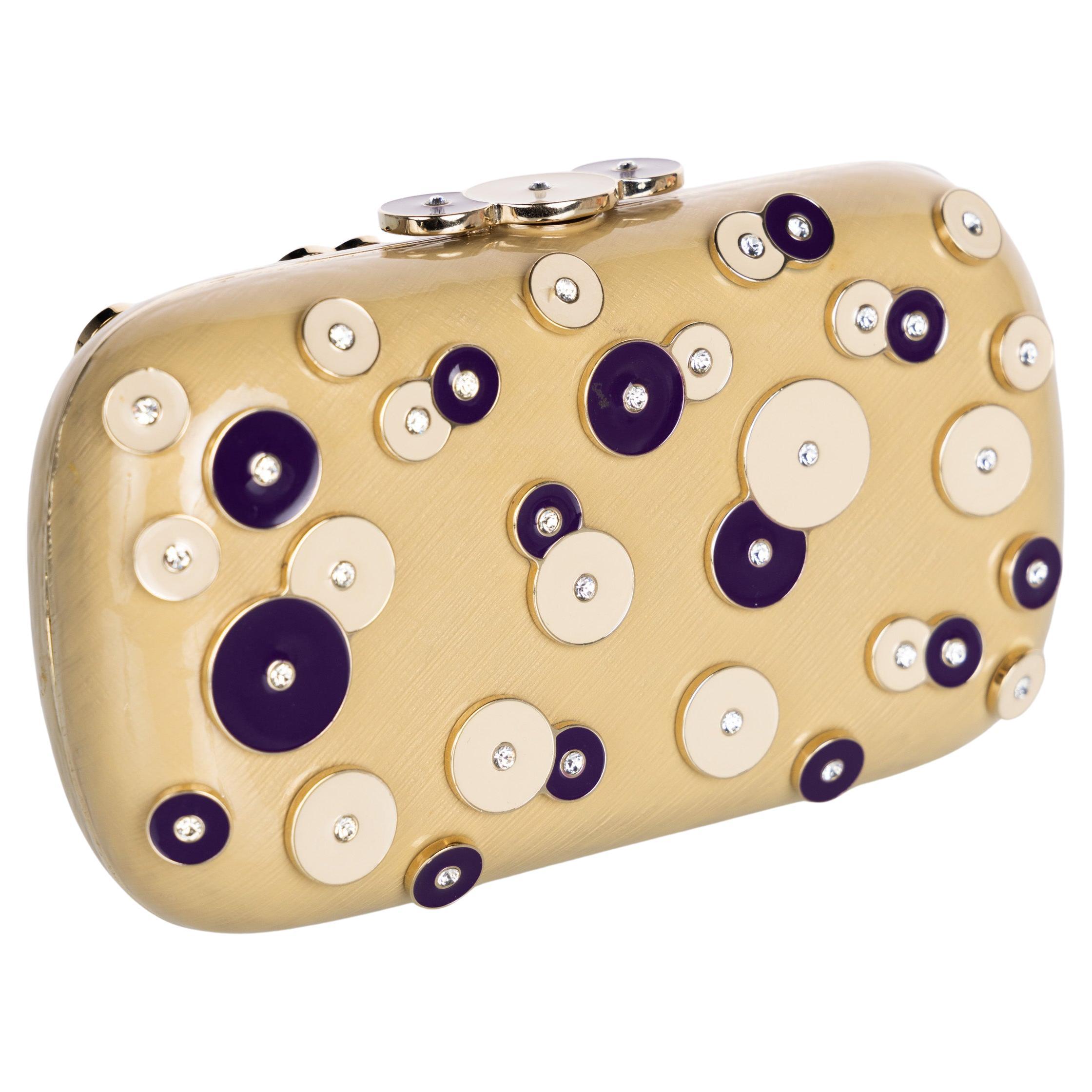 The Yves Saint Laurent by Tom Ford enamel clutch showcases the legendary designer's bold aesthetic. Its exterior features an enamel light gold base adorned with circular enamel accents in rich purple and cream, each embedded with crystal