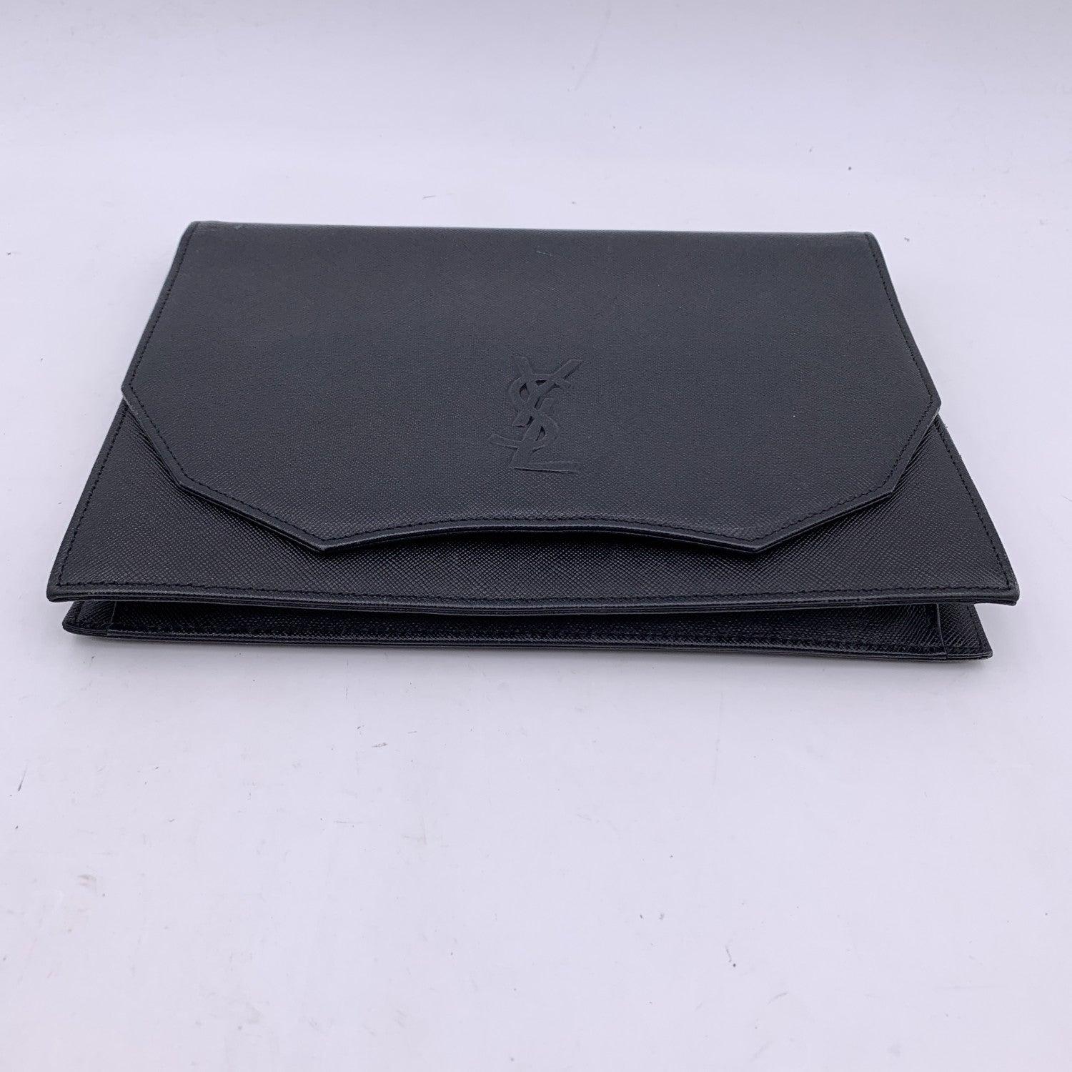 Pochette vintage Yves Saint Laurent, fabriquée en cuir noir. Il comporte un rabat avec une fermeture à bouton magnétique sur le devant. Logo YSL sur le devant. 1 poche arrière ouverte. Doublure en tissu noir. 1 poche latérale zippée à l'intérieur.