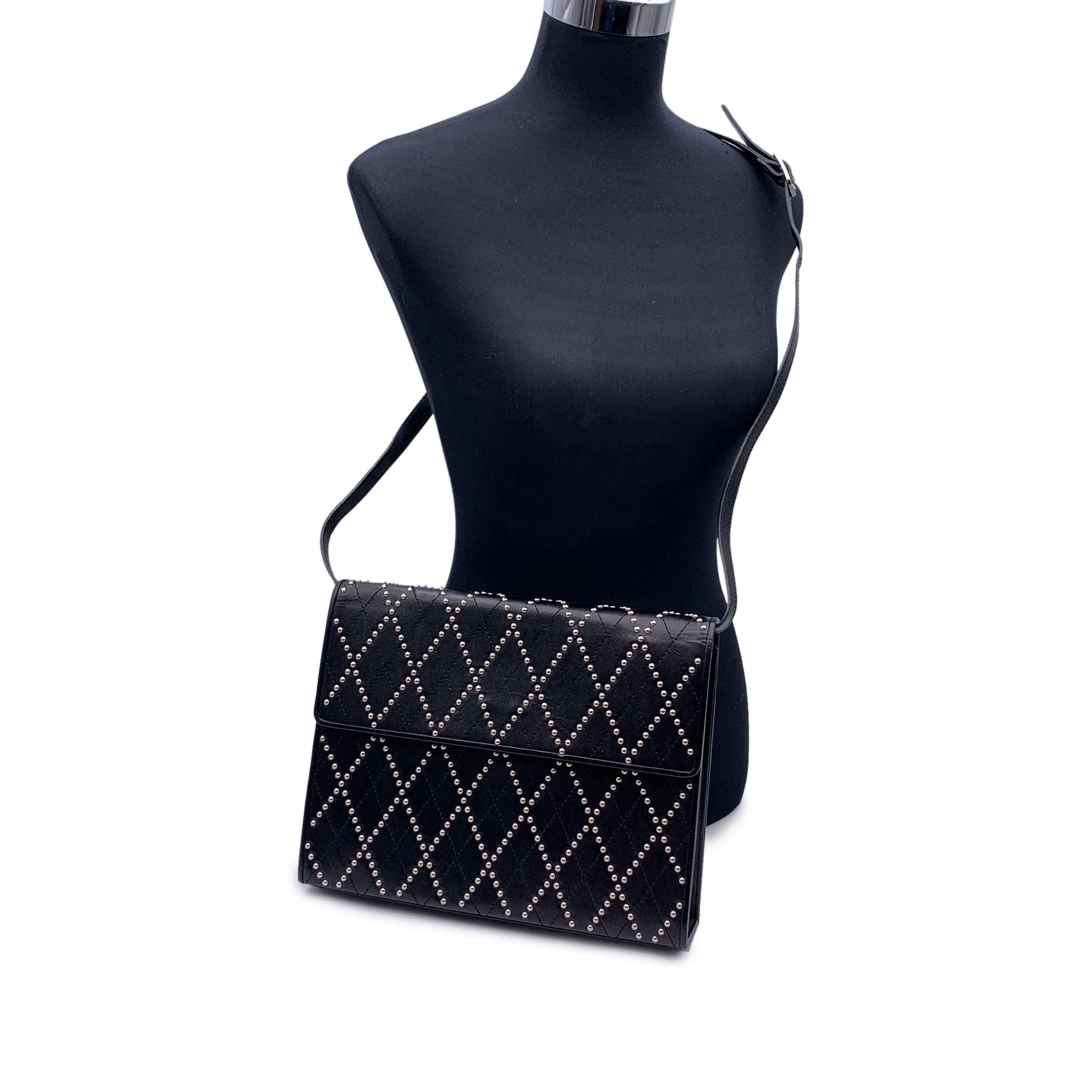 Bolso vintage Yves Saint Laurent de piel negra. Presenta un diseño acolchado y adornos de tachuelas de metal plateado con diseño de rombos. Solapa con cierre de botón magnético. 1 bolsillo abierto en la parte trasera. Forro de tela negra. 1 bolsillo