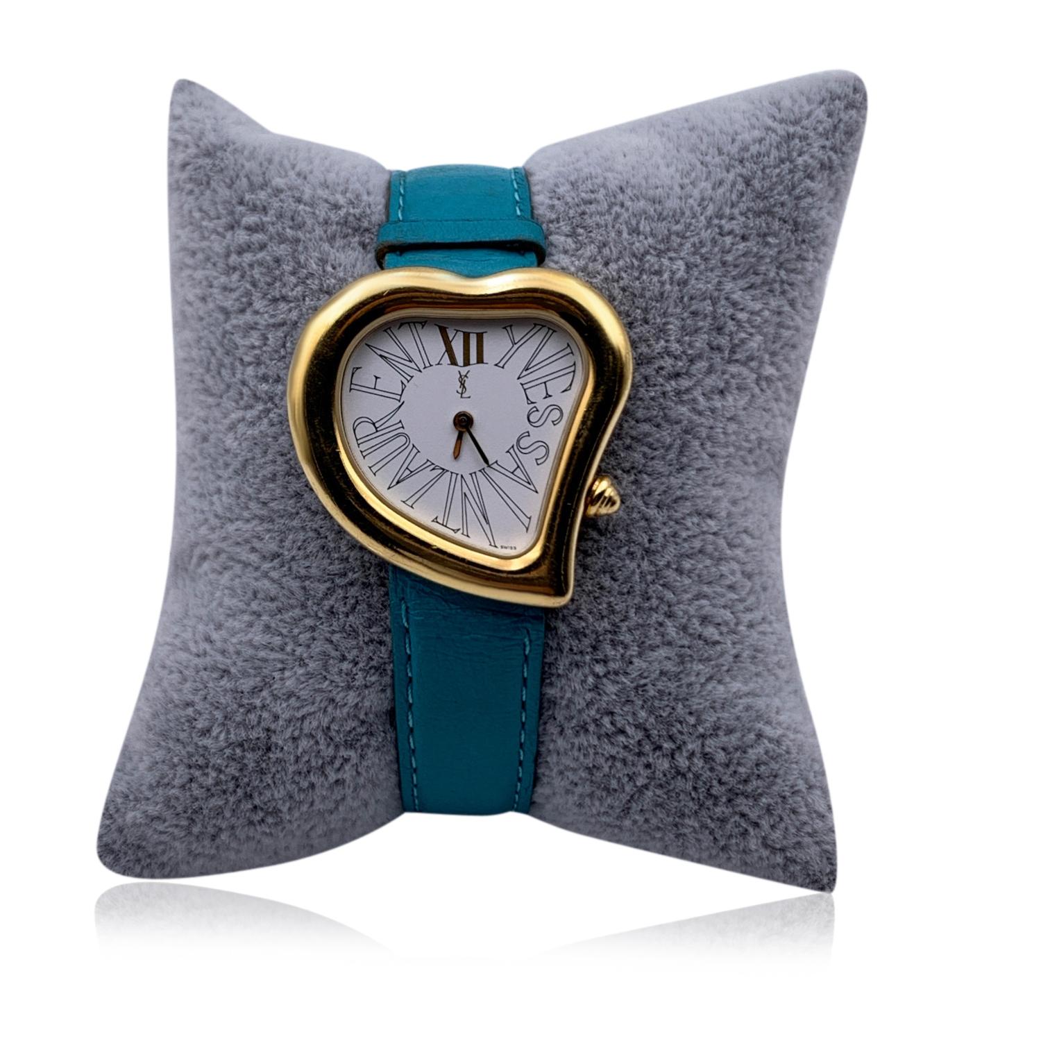Vintage Yves Saint Laurent heart-shaped wrist watch. Model 05F. Gold metal and stainless steel case (30 mm). White dial. Roman numbers. Turquoise leather strap with 8 holes adjustament. Not water resistant.Total length: 8 inches - 20.3 cm. Max