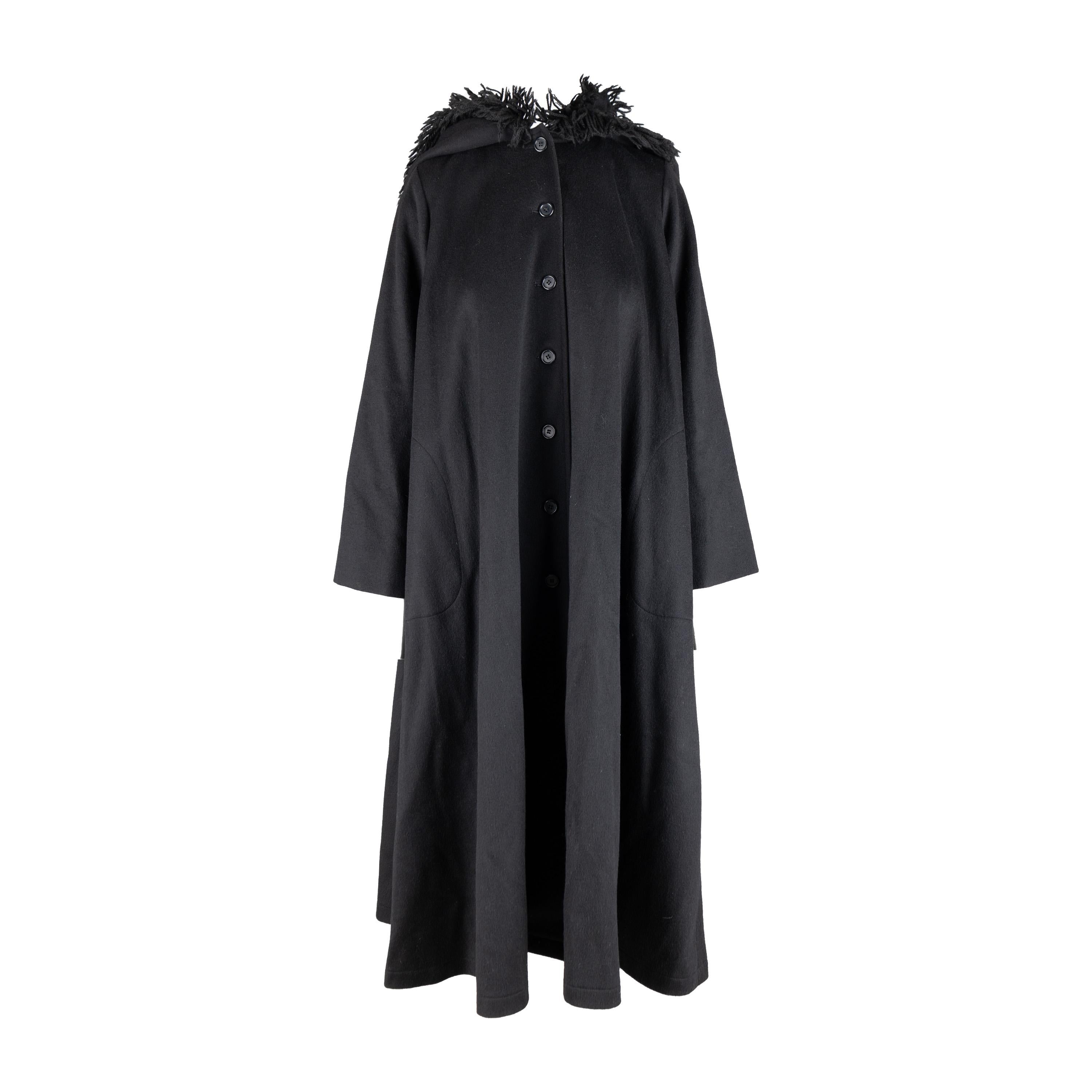 This is an iconic Yves Saint Laurent Vintage Hooded Cape Coat from the 1970's, crafted from wool. The black wool cape style coat features a hood and wool fringe trim. The coat underneath the cape has a swing silhouette with a button closure down the