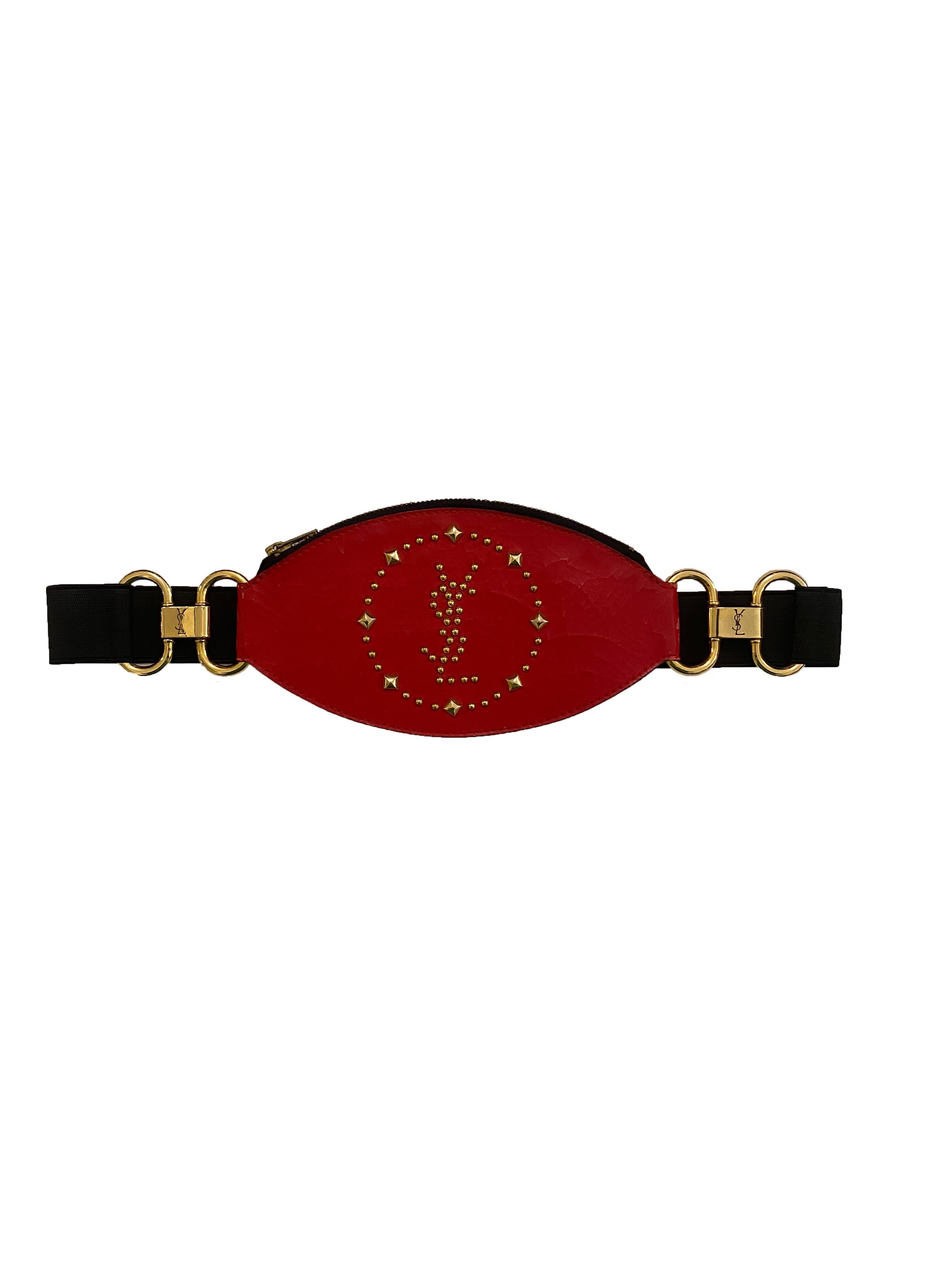 Vintage leather belt bag from Yves Saint Laurent. Made in France, 1980's. Cracked red leather pouch embellished with gold toned studs forming 'YSL' framed in a circle. Black elasticated waist belt clips together with gold toned metal hook clasp