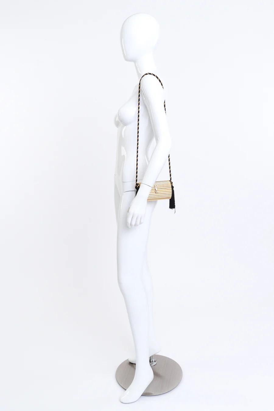 YVES SAINT LAURENT VINTAGE MINAUDIÈRE OPIUM BOX BAG GOLD METAL 1980s

This iconic YSL bag from the 1980’s has a rigid cylindric exterior made from shiny ribbed gold-tone metal. The bag features a long black and gold braided silk cord shoulder strap,