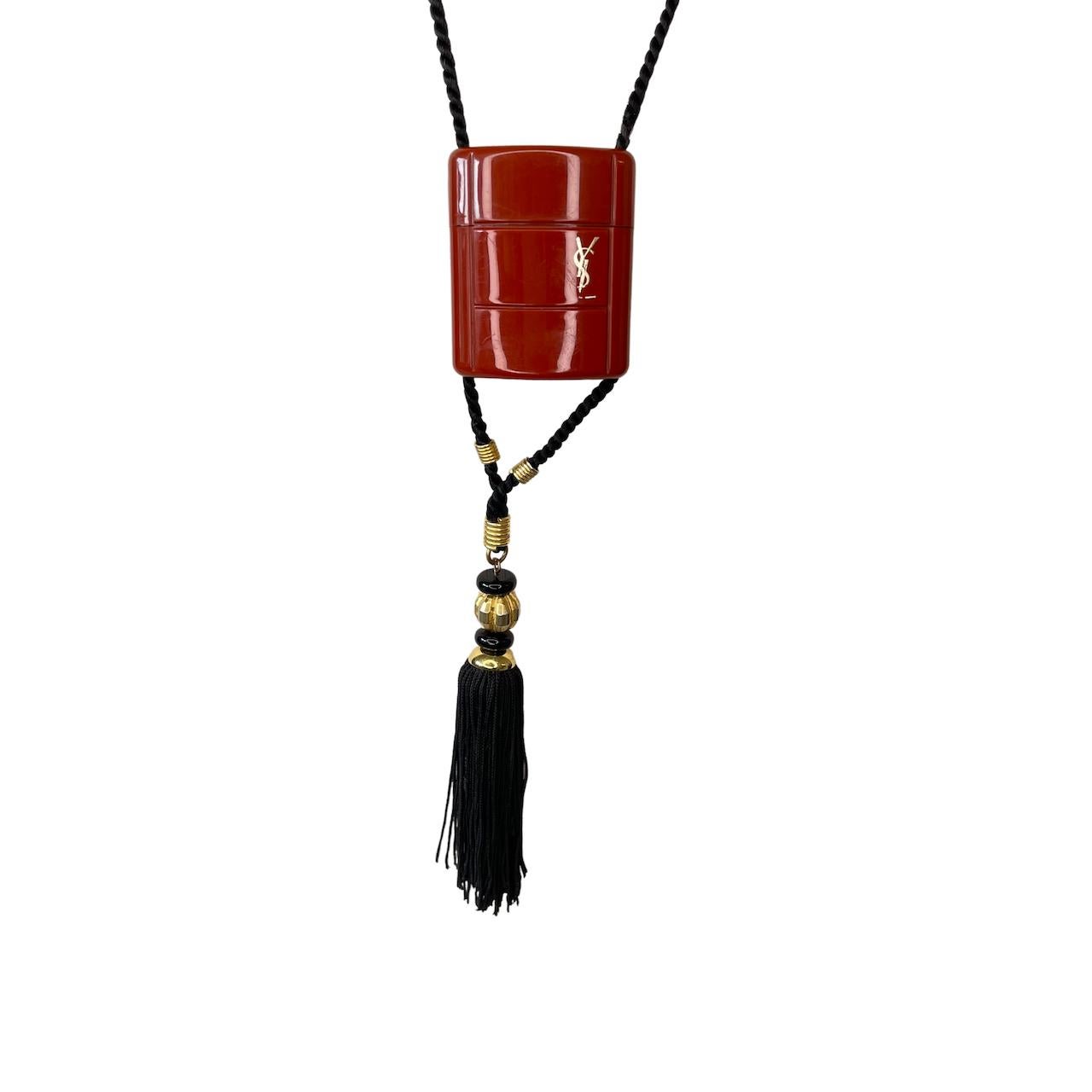 Saint Laurent, iconic, Opium perfume, pendent. Miniature, Opium perfume, flask, is made of an imitation Cinnebar, strung onto a black cord with a black tassel mixed with gold thread. Still contains some of the perfume in the flask.

COLOR: