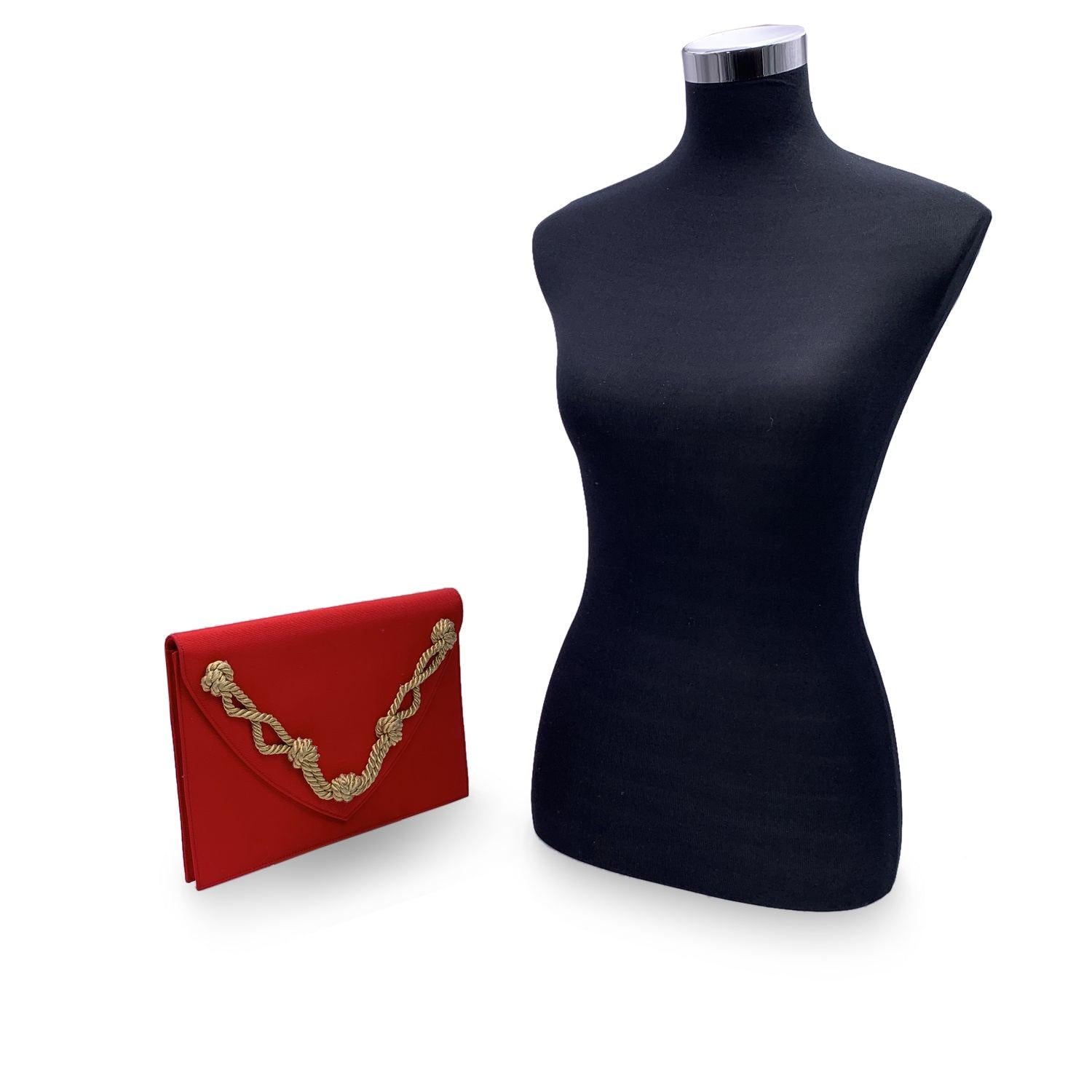 Yves Saint Laurent vintage clutch bag, crafted in red gros-grain fabric. Beutiful gold tone knotted cord on the flap. It features a flap with magnetic button closure on the front. Fabric lining. 1 side zip pocket and 1 side open pocket inside. 'YVES