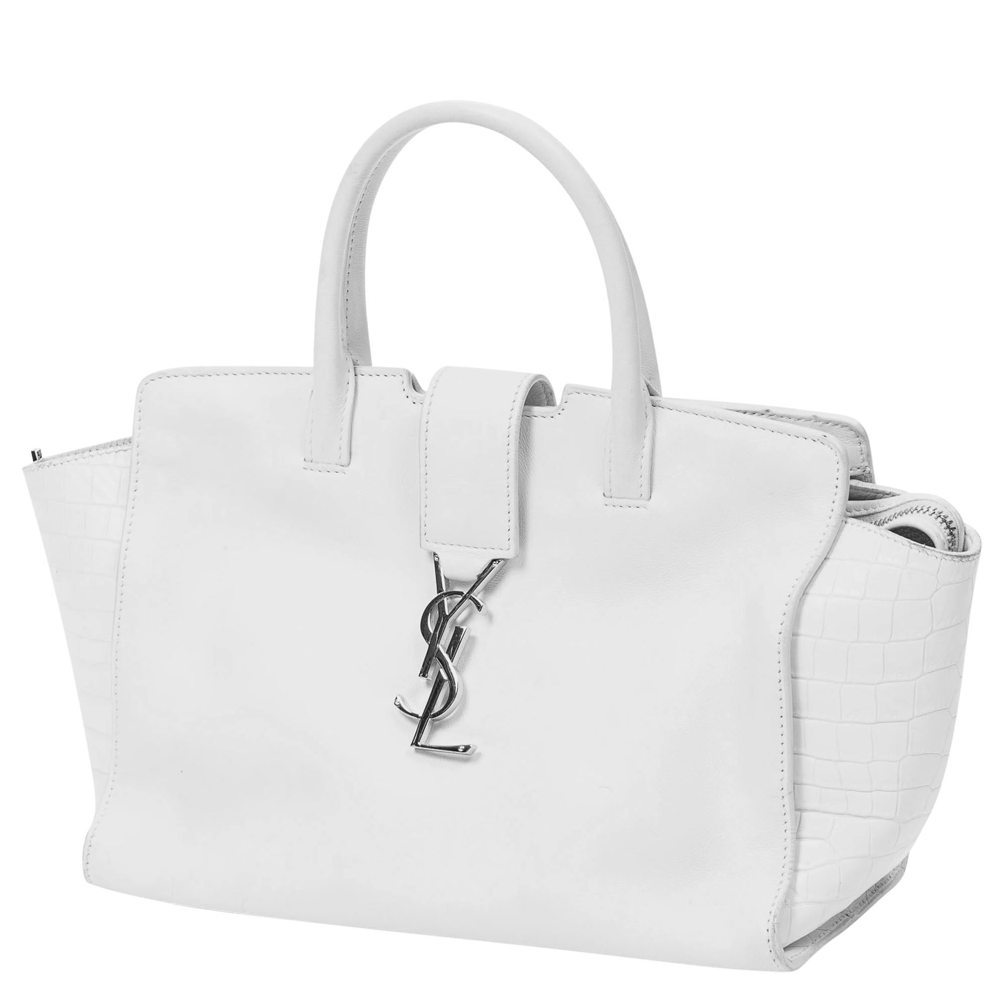Elevate your ensemble with the Yves Saint Laurent White Logo Tote. Crafted from premium calfskin leather in pristine white, it exudes timeless elegance. Adorned with silver-tone hardware and featuring a practical zipper closure, its leather-lined