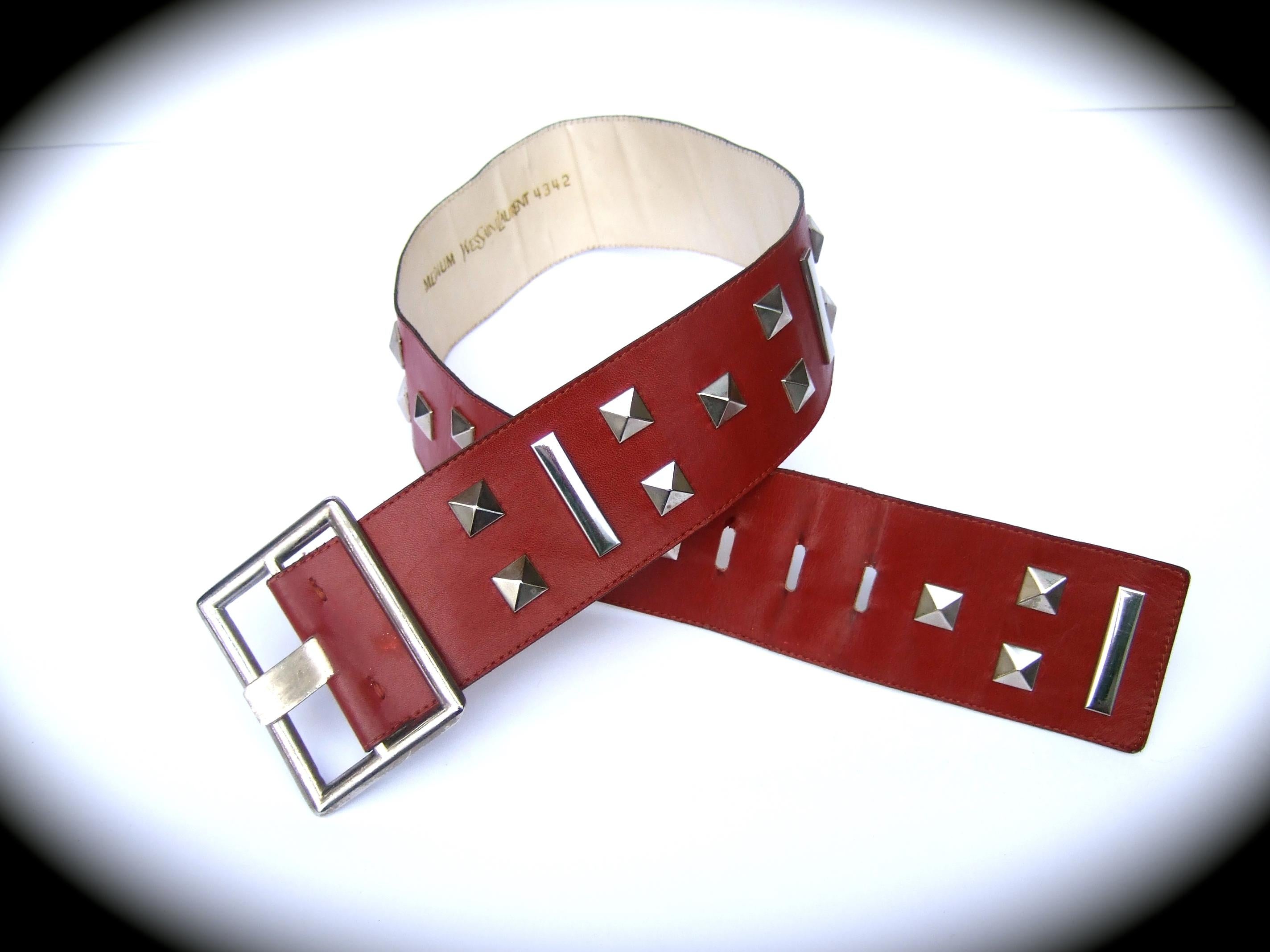 Yves Saint Laurent Red leather chrome grommet studded belt c 1970s

The wide dark red leather belt is designed with a series of chrome metal grommets; juxtaposed with rectangular vertical metal embellishments. Paired with a large chrome metal
