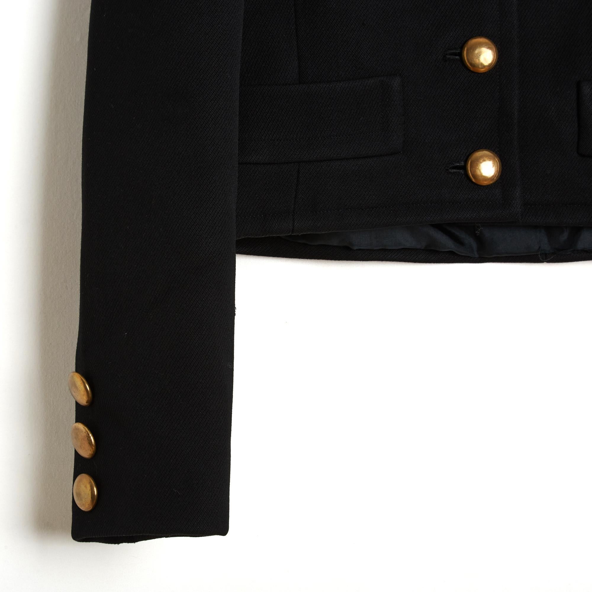 Yves Saint Laurent Haute Couture Jacke um 1970 aus dickem schwarzem Wollstoff, gerader Schnitt, kleiner Stehkragen, der mit 6 goldenen Metallknöpfen geschlossen wird, 2 Schlitztaschen in der Taille, lange Ärmel mit 3 koordinierten Zierknöpfen. Keine