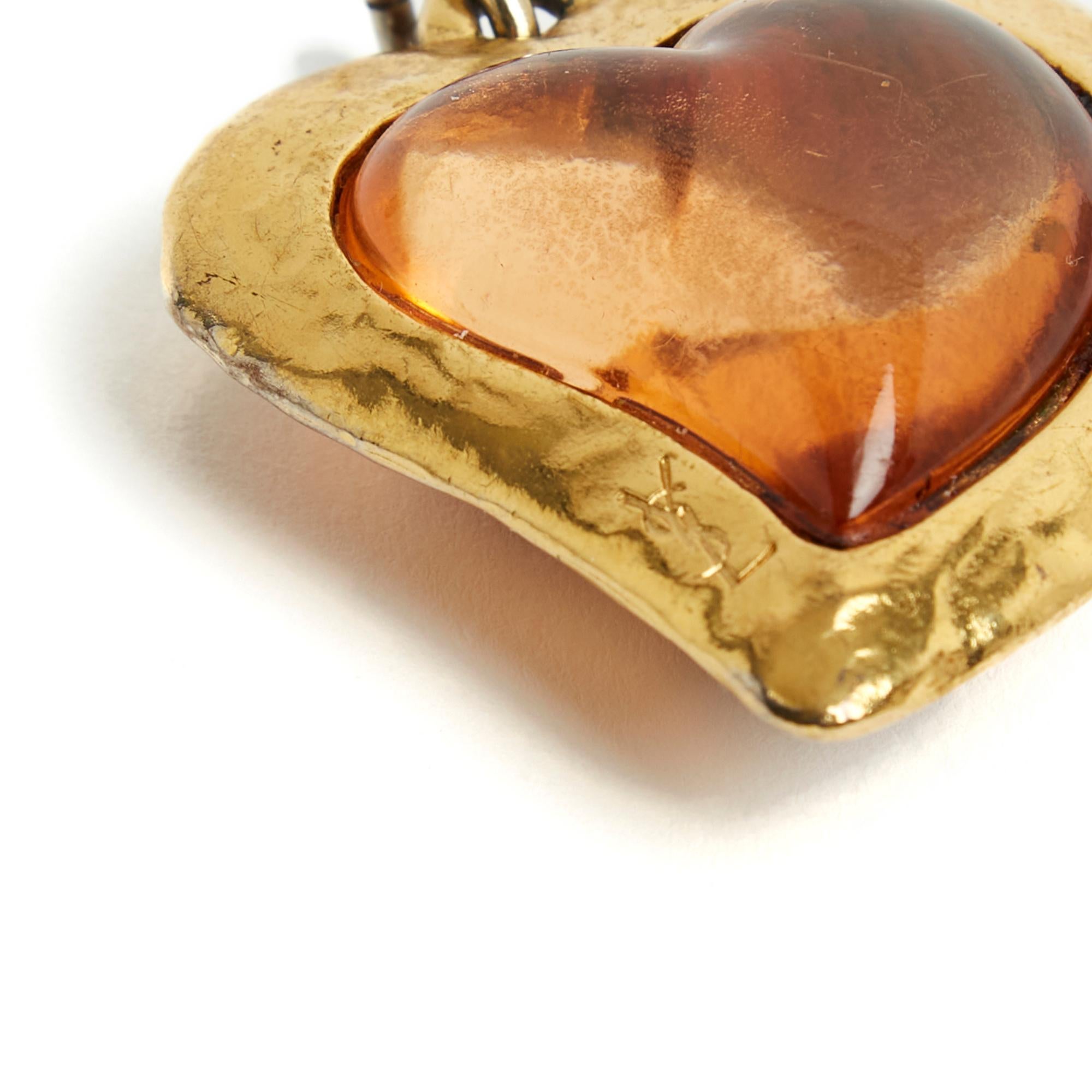 Yves Saint Laurent pendant with the motif of a heart in amber-colored resin surrounded by gold metal with the Yves Saint Laurent logo, bail for chain or cord. Width 4 cm x height 4.5 cm. The heart is very vintage but it is charming, delivered on a