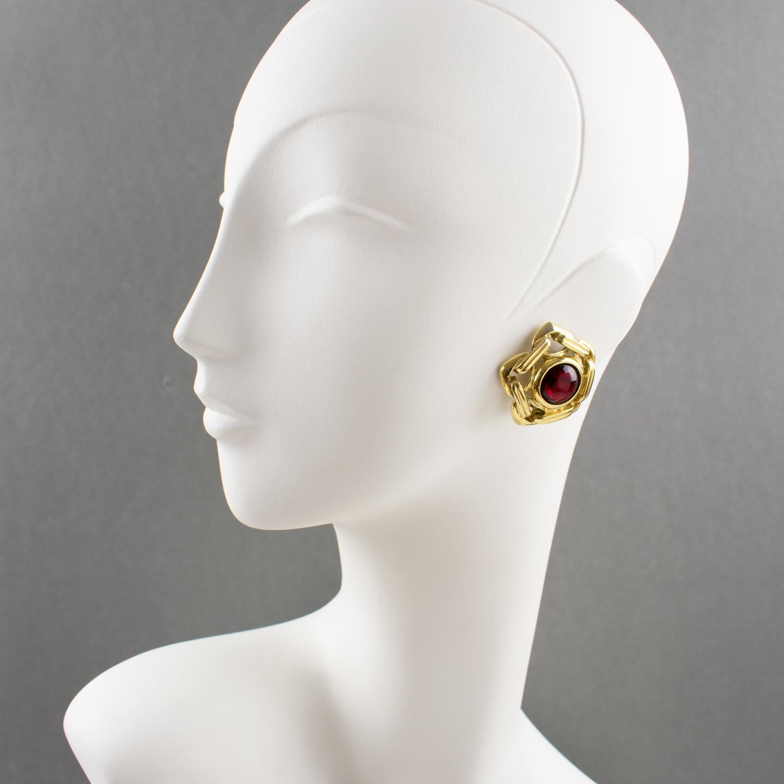 Beautiful Yves Saint Laurent YSL Paris clip-on earrings. Gilt metal hexagonal dimensional shape, metal all textured and see-thru featuring large chain compliment with ruby red resin cabochon rhinestone. Signed at the back with pierced 'YSL' logo on
