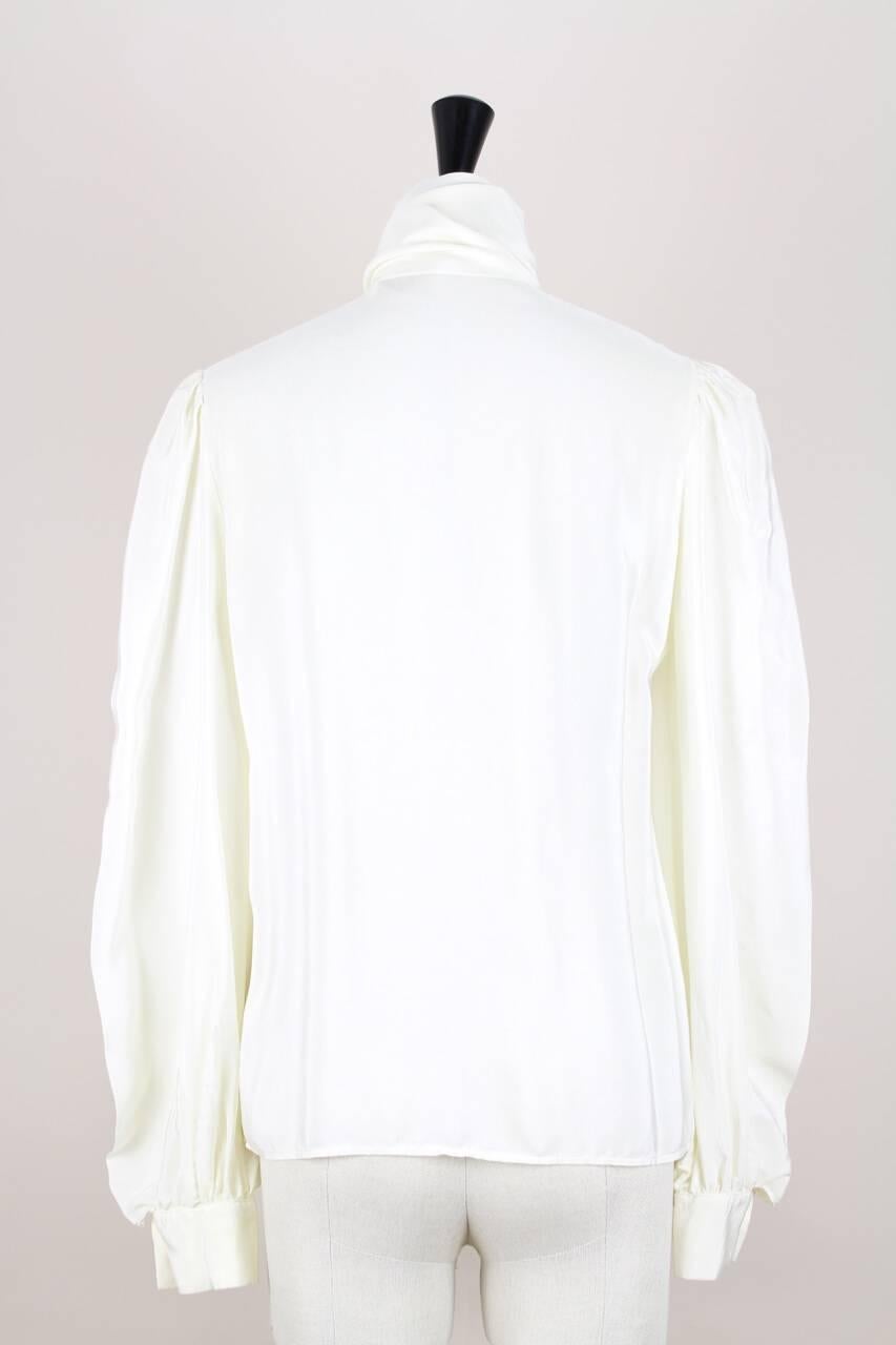 This is a beautiful and classic straight cut silk blouse by Yves Saint Laurent in a cream hue. There are all the YSL signature touches - the slightly gathered shoulder and the high neck with its long tie (see picture 7) that is built right into the