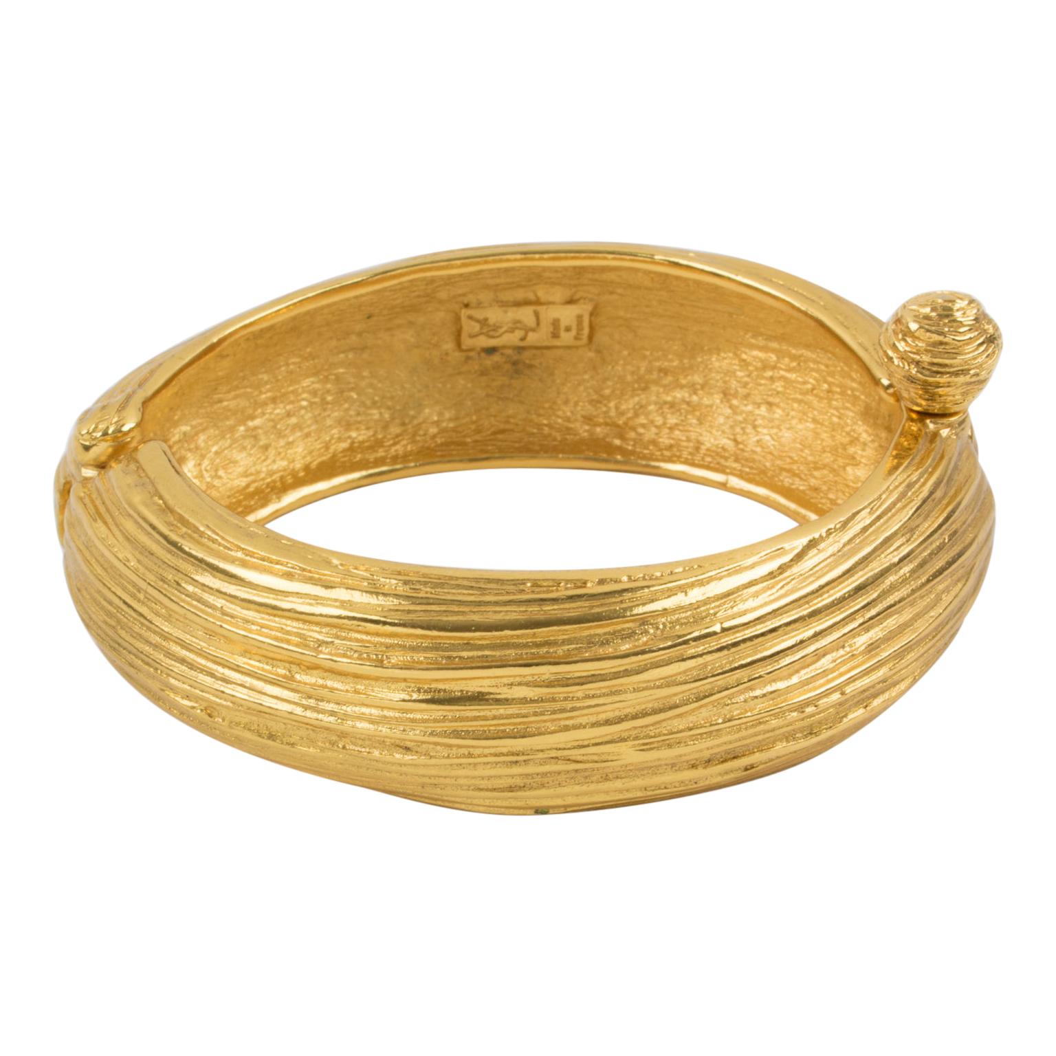 Yves Saint Laurent YSL Paris designed this couture clamper bracelet. The piece features a massive oval shape in gilded metal with all carving and striped texture patterns. The bracelet has a hinge and opens with a push/pull stick lock closure. The
