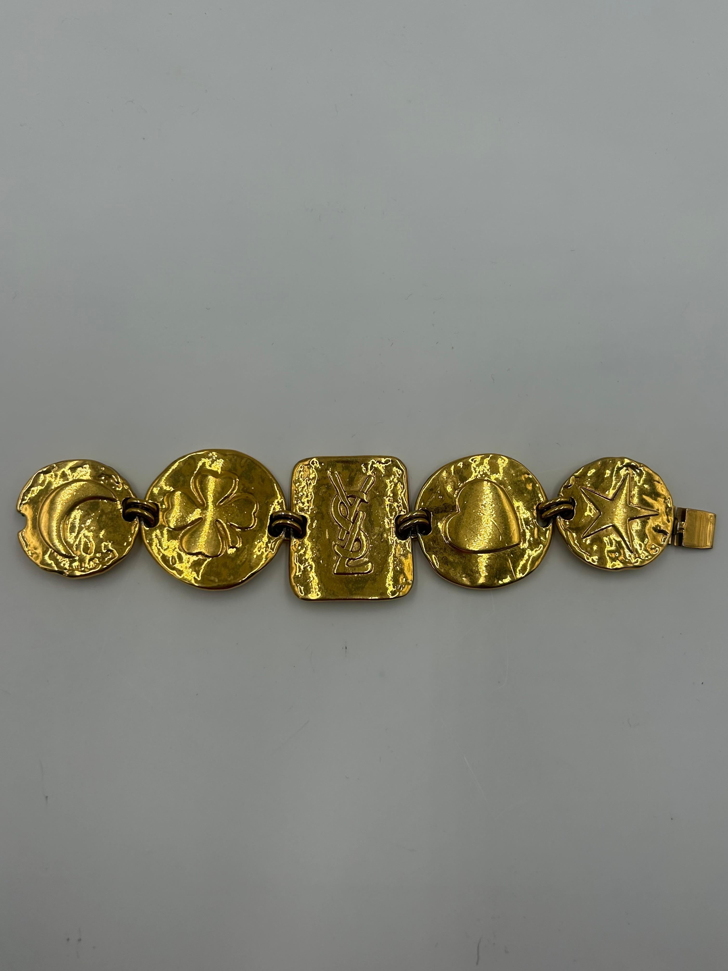 Il bracciale YSL in oro è un accessorio di grande effetto ed eleganza che incarna lo spirito audace e glamour del marchio Yves Saint Laurent. Realizzato in metallo lucido con una ricca finitura dorata, il bracciale presenta l'iconico logo YSL a