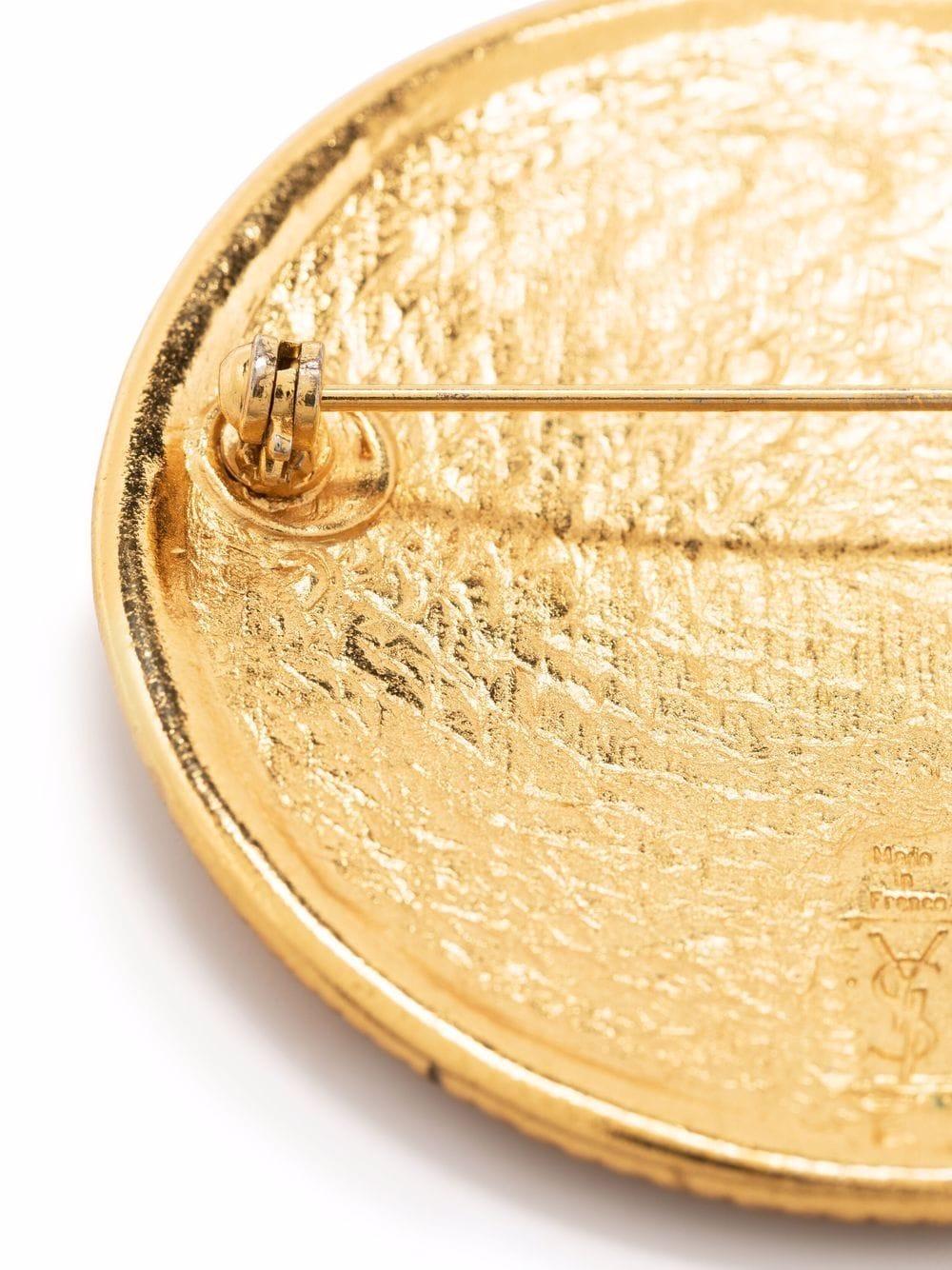  Broche à logo Yves Saint Laurent des années 1990, en métal doré, avec un logo YSL décoratif,  une épingle de sûreté arrière. 
Diamètre : 4,5 cm (1,7in.)
En bon état vintage.  Fabriqué en France. 
Nous garantissons que vous recevrez cet article