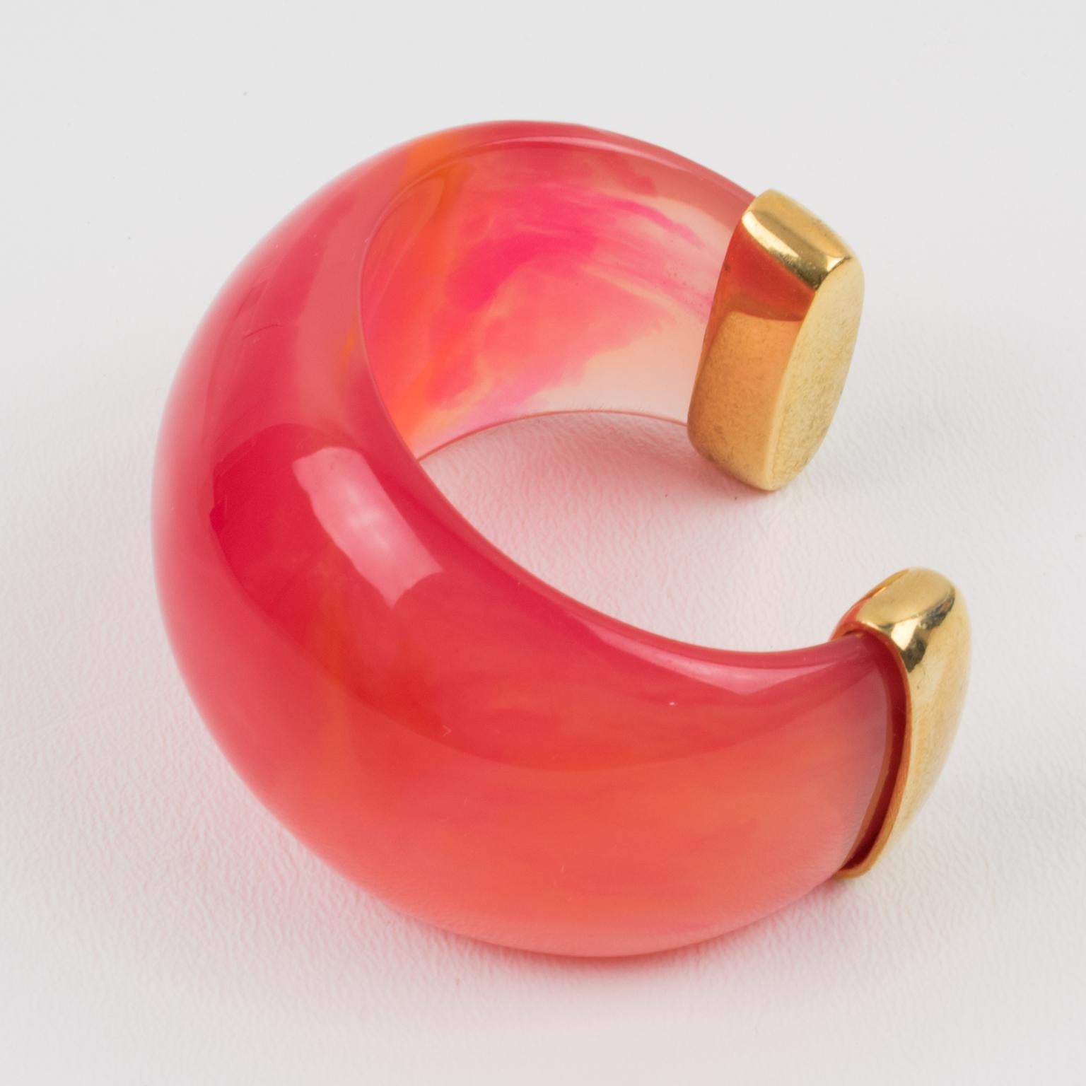 Exquisite Yves Saint Laurent YSL Paris cuff bracelet. Massive resin bracelet, featuring a heavily domed cuff in translucent pink tequila sunrise marbled resin finished with gilt metal hardware. Tequila sunrise color is a beautiful bright pink tone