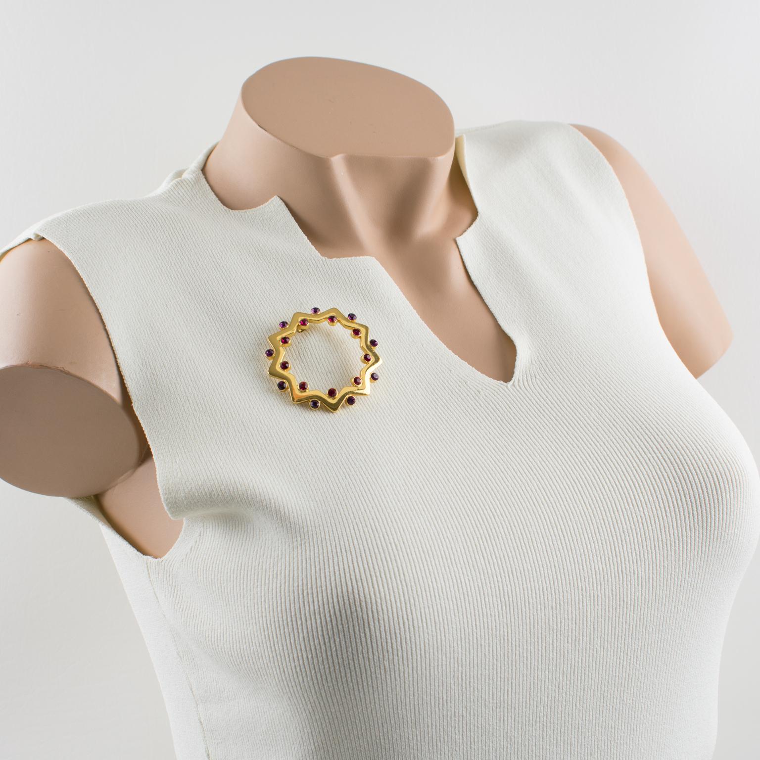 Cette ravissante broche bijou Yves Saint Laurent YSL Paris présente une étoile géométrique en métal doré, sculptée et transparente, ornée de strass en cristal de couleur violette et rouge rubis. Le pin's est signé au dos avec le logo YSL, Made in