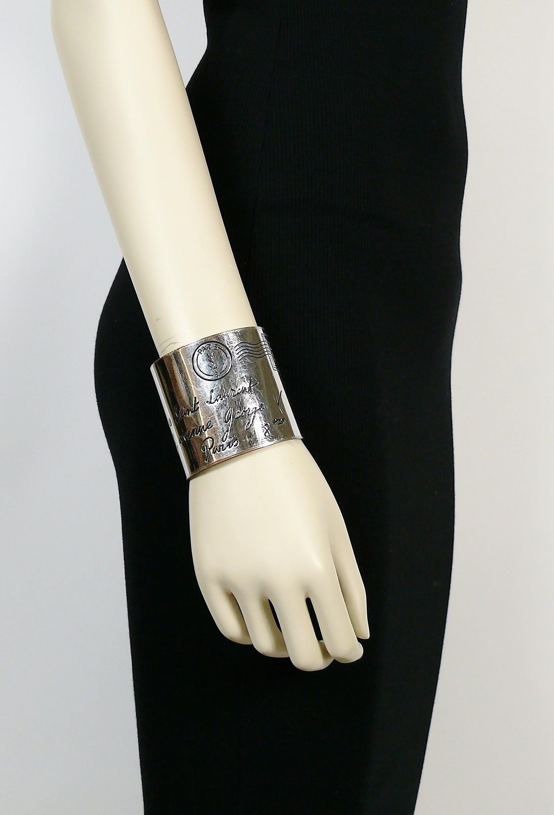 YVES SAINT LAURENT rare silver toned address postcard cuff bracelet engraved in black enamel YVES SAINT LAURENT 7, Avenue George V, Paris 8eme.

Engraved postal stamp at the top.

Indicative measurements : inner circumference approx. 18.54 cm (7.30