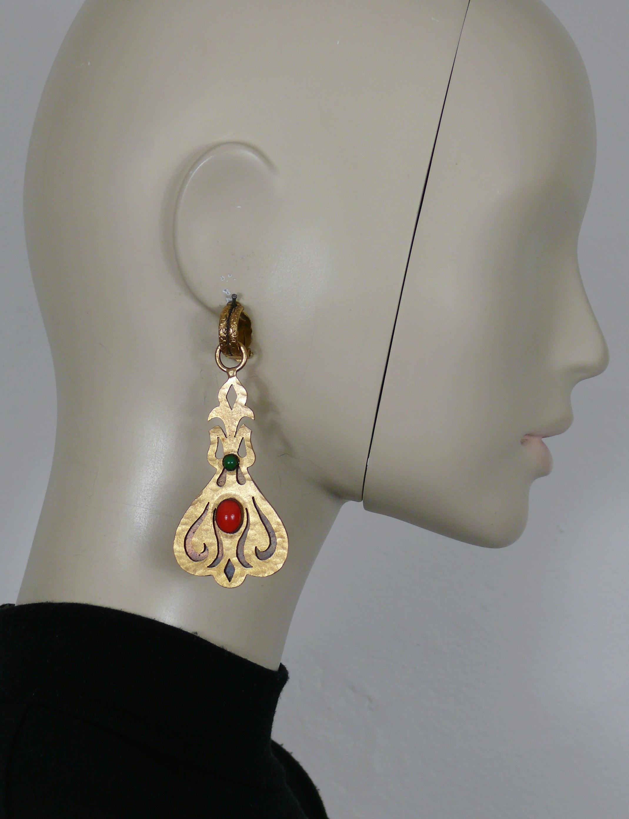 YVES SAINT LAURENT Jugendstil-inspirierte, strukturierte, goldfarbene Ohrringe (Clip-on) mit einem orangefarbenen Glascabochon und einem grünen Kunstharz-Cabochon.

Geprägtes YSL.

Ungefähre Maße: Höhe ca. 8,5 cm (3,35 Zoll) / max. Breite ca. 3,6 cm