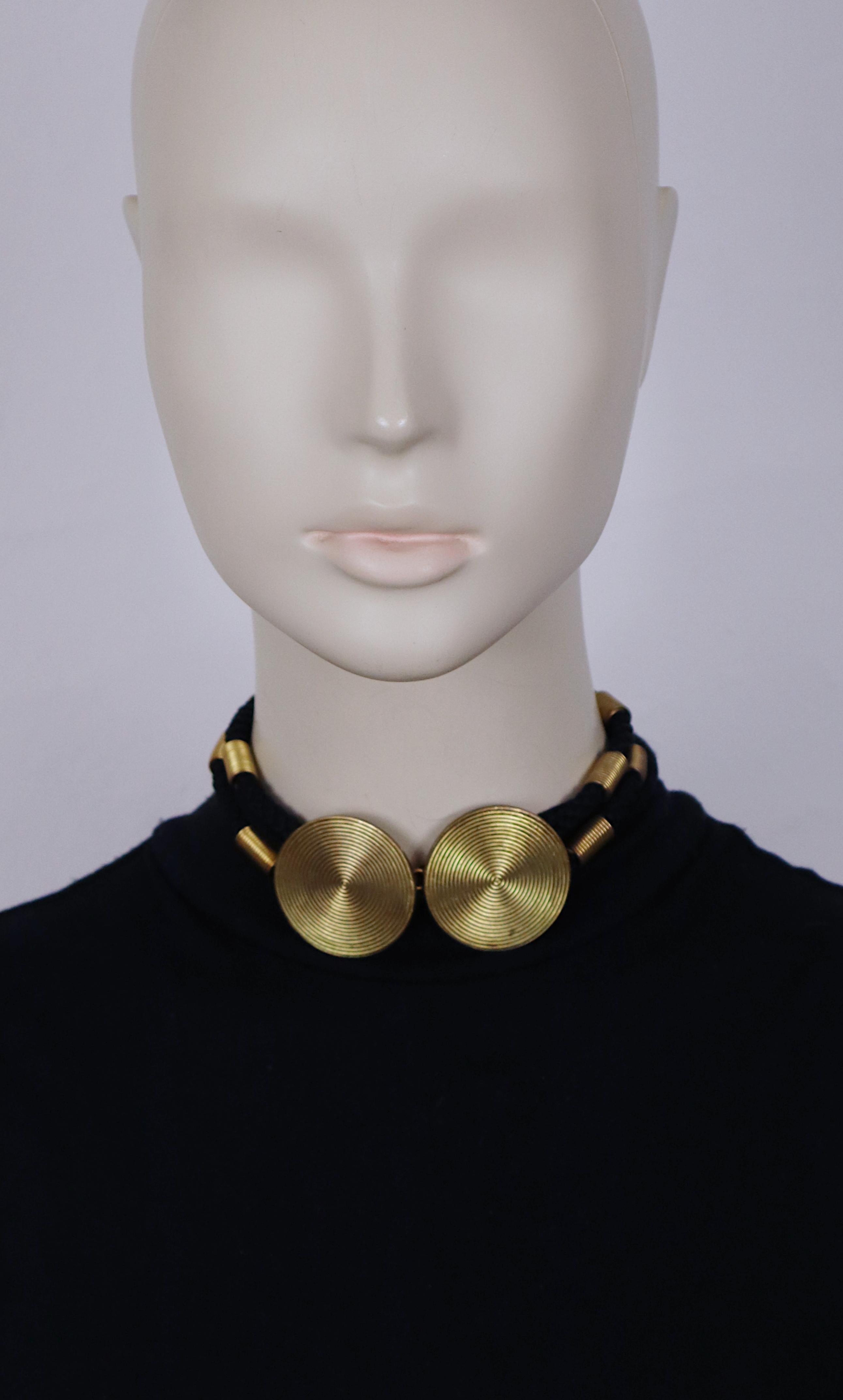 Collier ras de cou en corde tressée noire vintage YVES SAINT LAURENT, orné de détails en forme de ressort en ton or vieilli et de deux disques concentriques tourbillonnants.

Fermeture par un crochet.

Embossé YSL.

Mesures indicatives : longueur