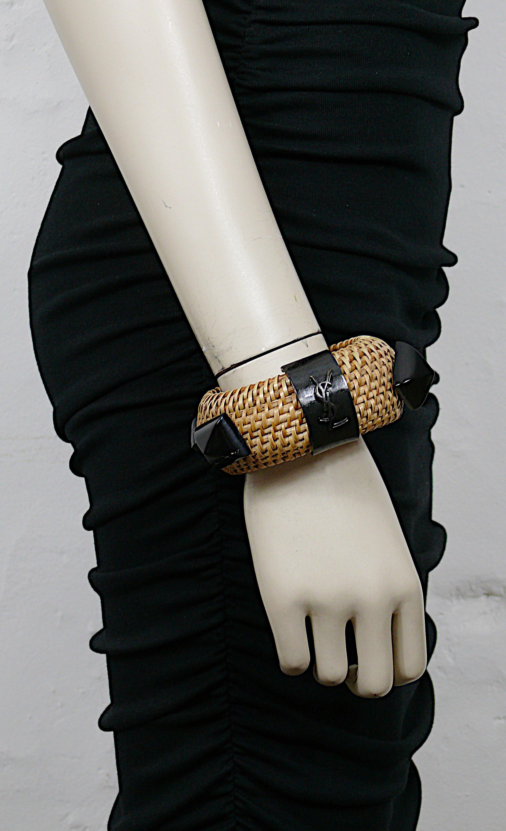 Bracciale in vimini naturale intrecciato di Yves Saint Laurent impreziosito da cabochon in resina di finto corno (colore nero marmorizzato) e da un anello con firma in metallo color bronzo invecchiato.

Logo YSL sull'anello in metallo color