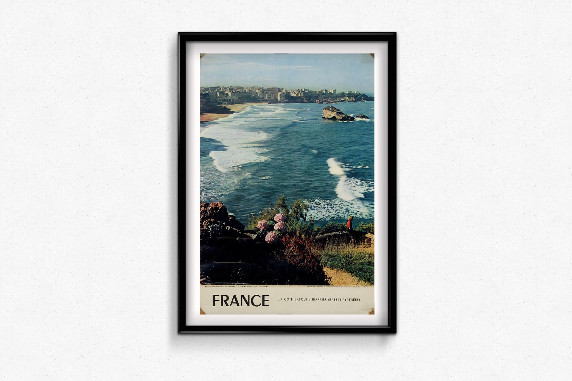 This luminous 1956 photographic travel poster by Yvon captures the timeless elegance of Biarritz, the “Queen of Beaches” on France’s Basque coast. In the foreground, wild hydrangeas bloom above the Atlantic surf, while a solitary figure gazes