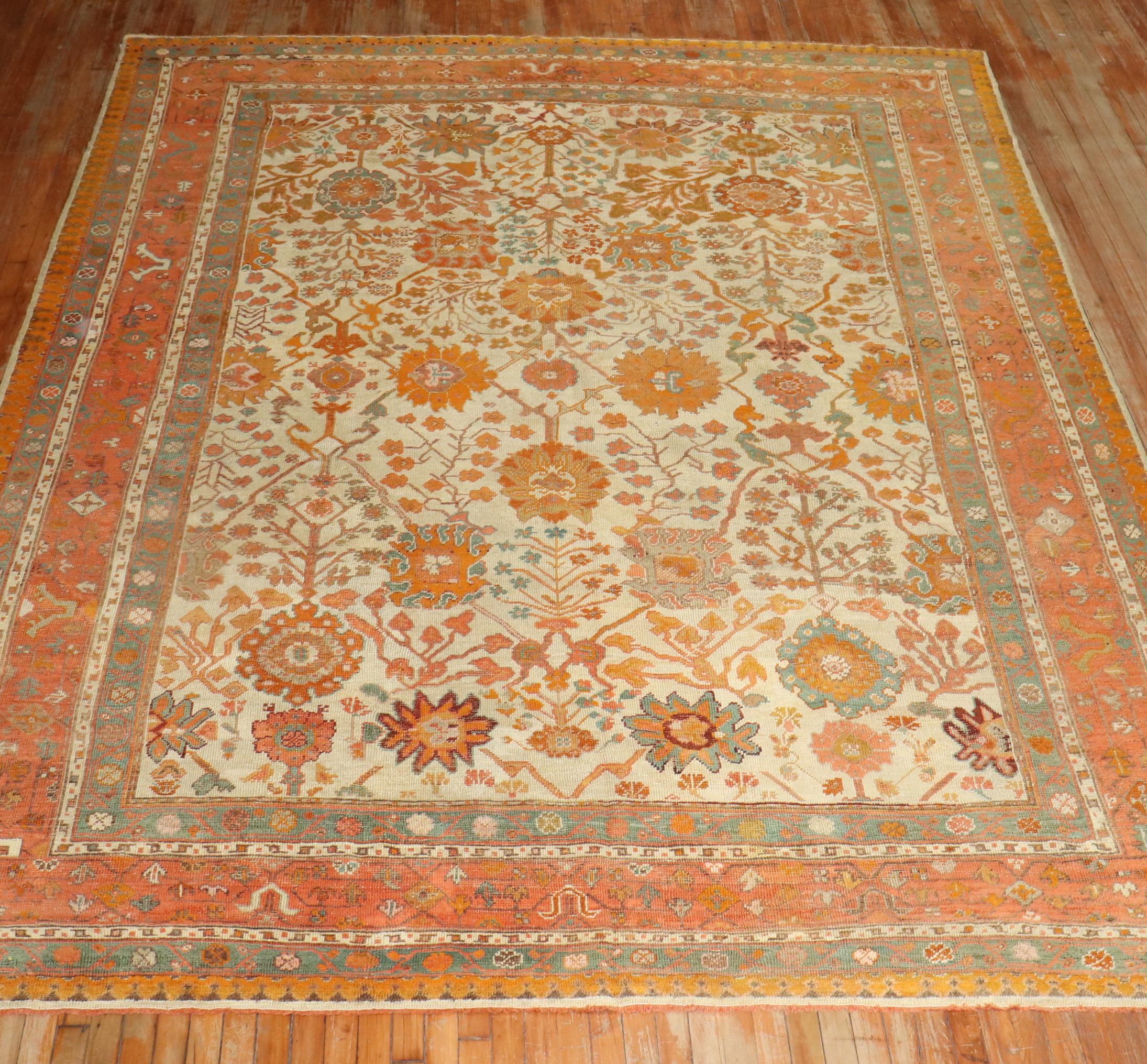 An early 20th-century room size Antique Turkish Oushak rug in predominantly ivory and orange with teal and brown highlights

Measures: 9'4'' x 11'

Oushak rugs originated in the small town of Oushak in west-central Anatolia, today just south of