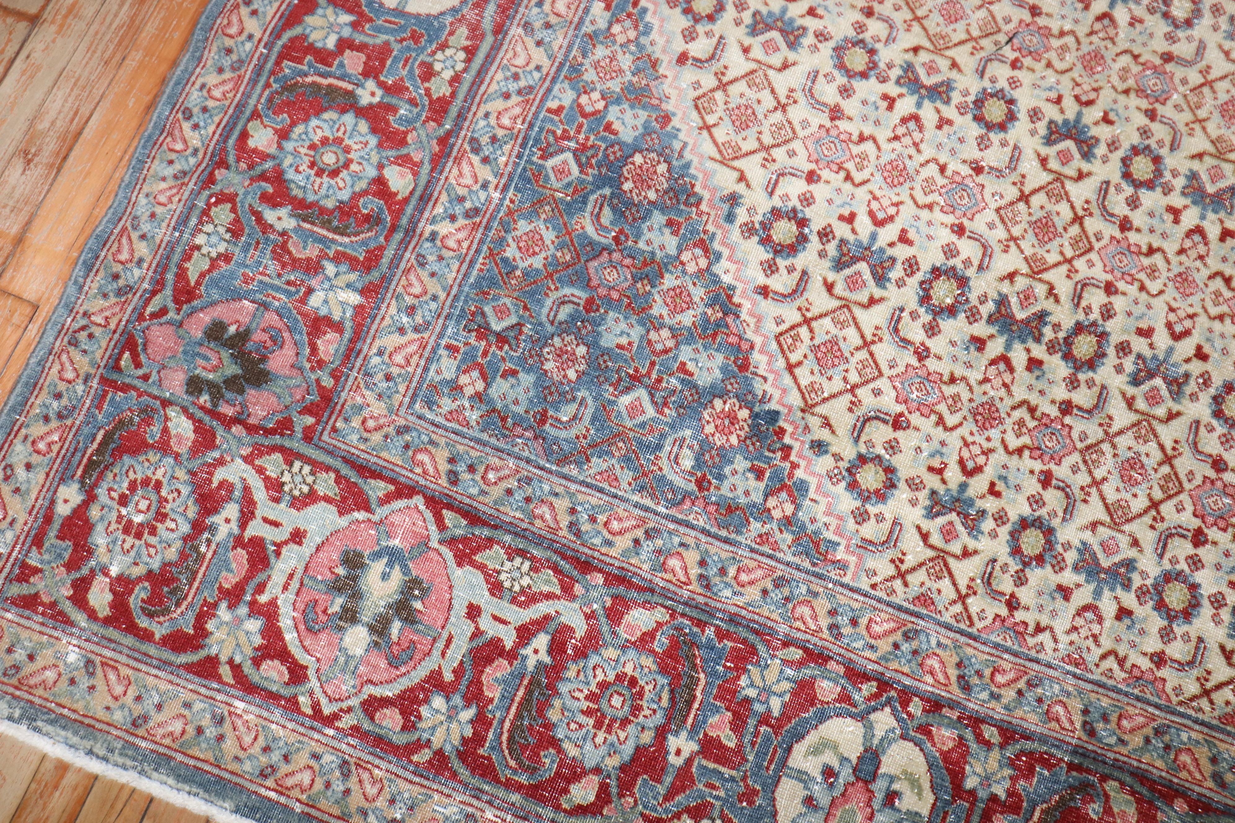An early 20th century Room size Persian Tabriz worn rug with a small light blue central medallion on a herati design wheat ground.

Measures: 9'6'' x 13'6''.