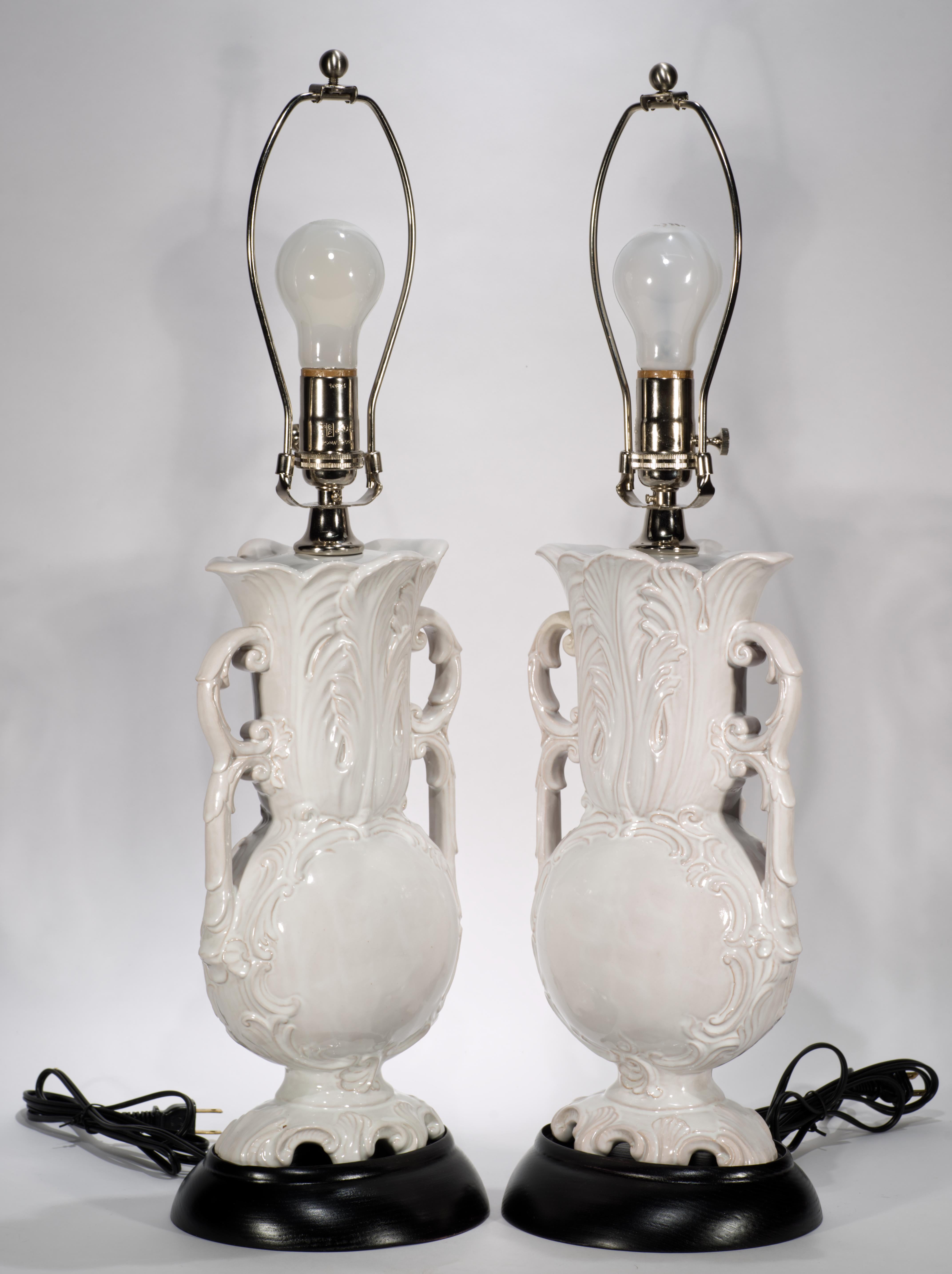 Paire de lampes de table vintage en forme d'urne avec des poignées doubles ornées et des corps en céramique très détaillés avec des reliefs de feuilles et des bases larges texturées. Le blanc vif de la glaçure majolique monochromatique accentue les