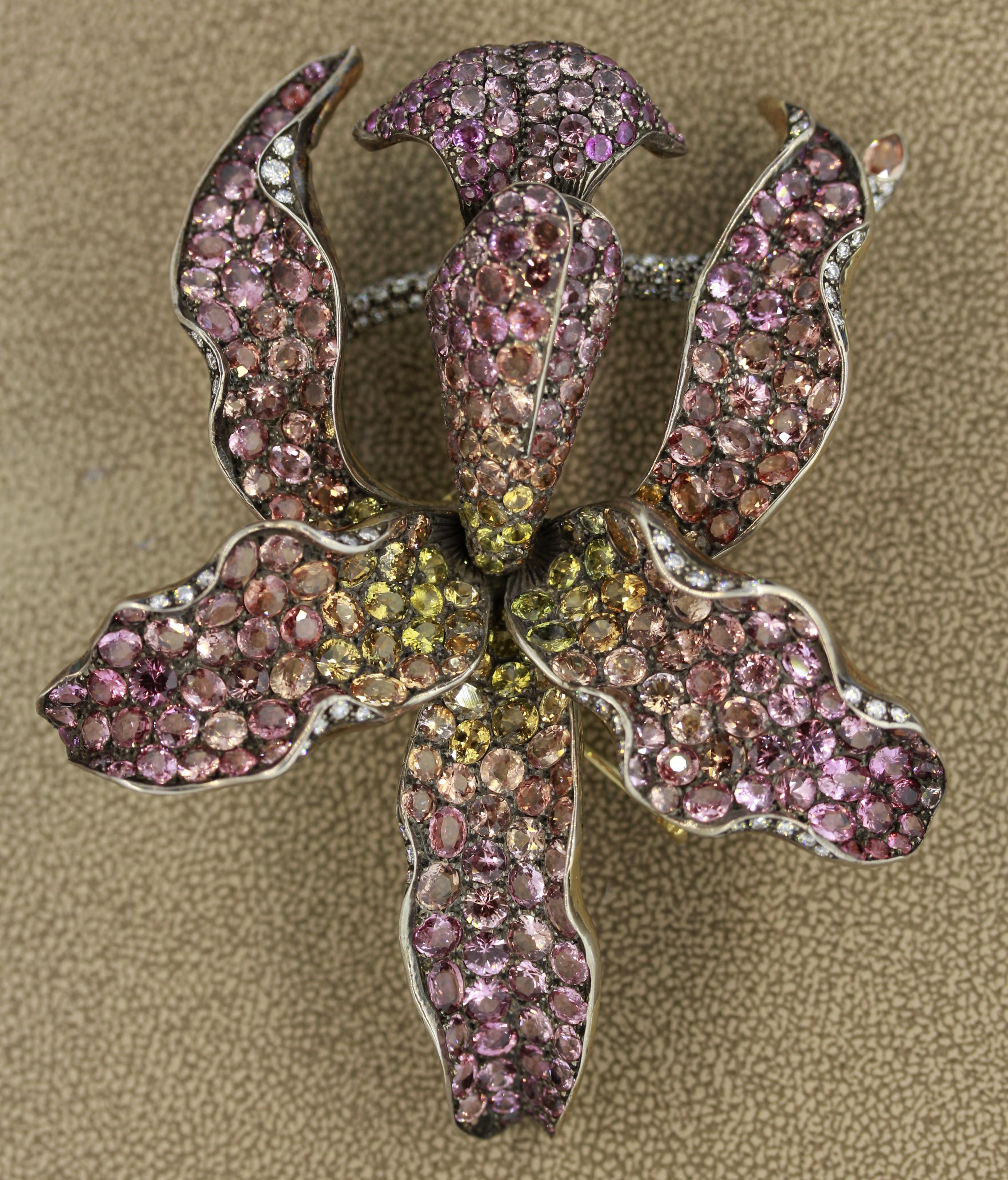 A magnificent and large gold brooch depicting a colorful orchid in full blossom. It features 44 carats of Padparadscha sapphires with a mesmerizing orangy-pink color along with yellow sapphires closer to the center of the flower. The stem of the
