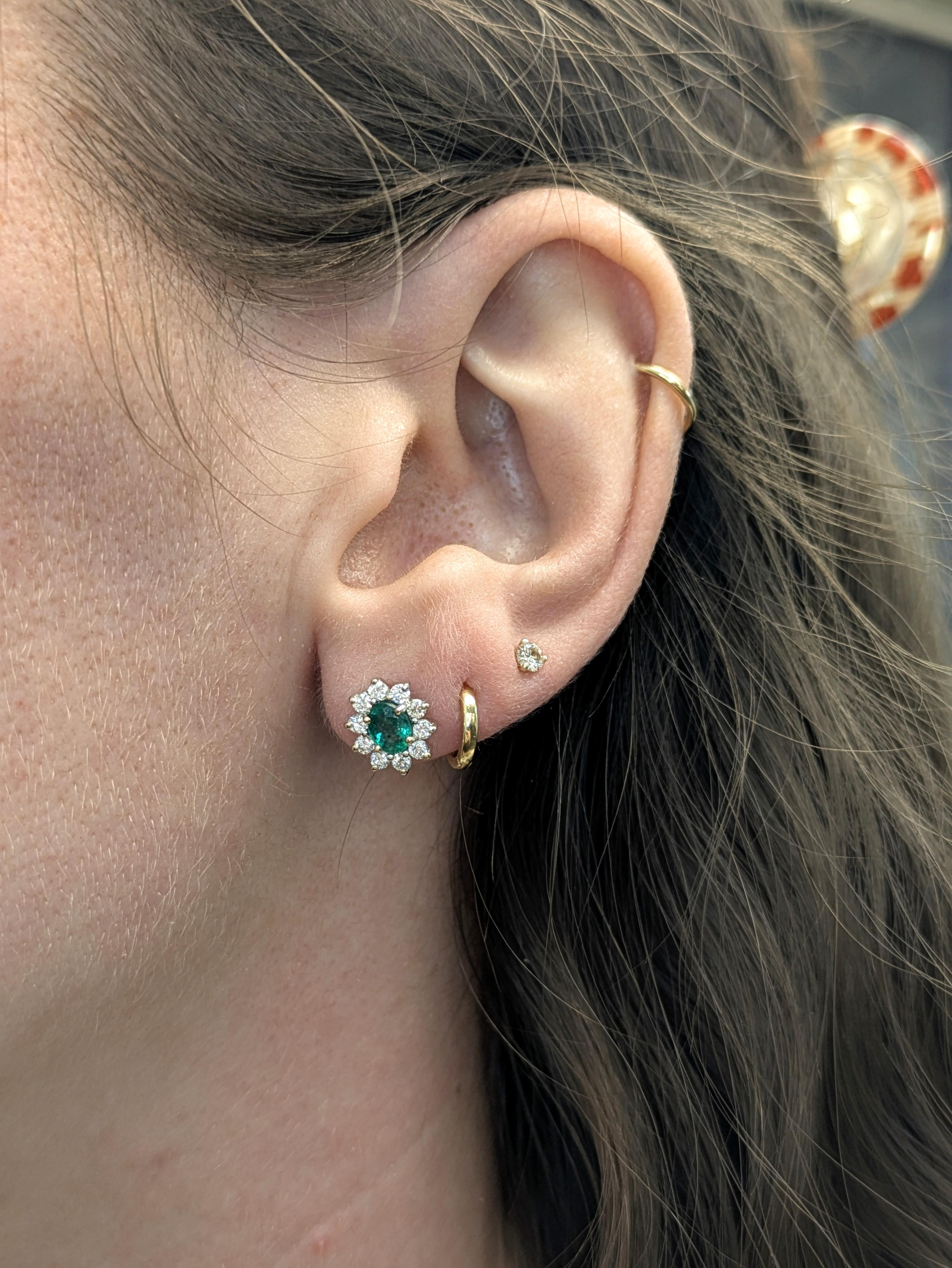 Estos pendientes ovalados de esmeralda de Zambia irradian una belleza atemporal. Rodeada por un halo de diamantes extraídos de la tierra en un delicado diseño de flor en forma de rayo de sol, cada esmeralda verde vibrante está engastada en oro