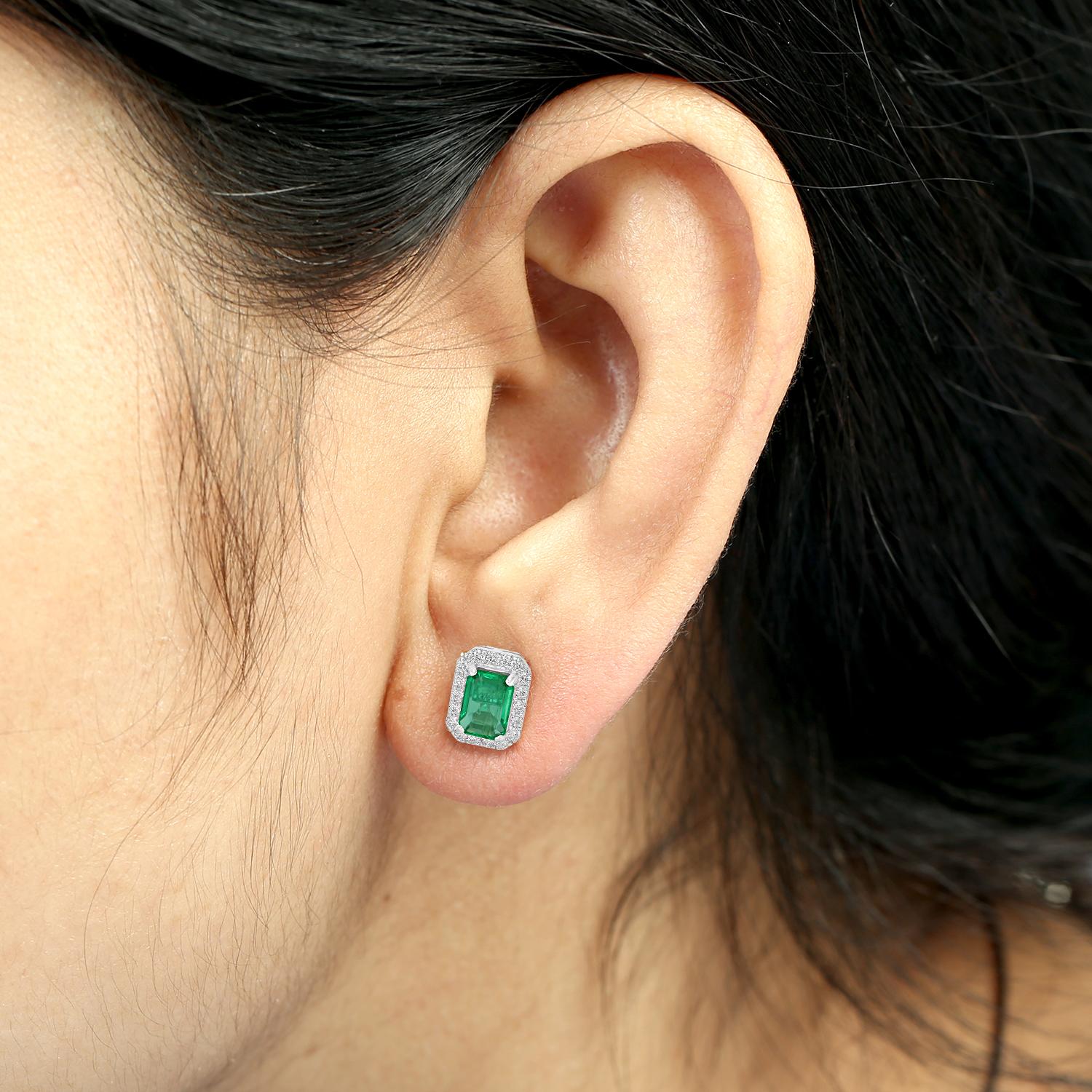 Ces boucles d'oreilles minimales et raffinées sont ornées d'émeraudes de Zambie vibrantes, rehaussées d'un halo de diamants subtil pour un look propre et classique. Conçues en or blanc 18 carats, elles offrent un mélange parfait de couleur et
