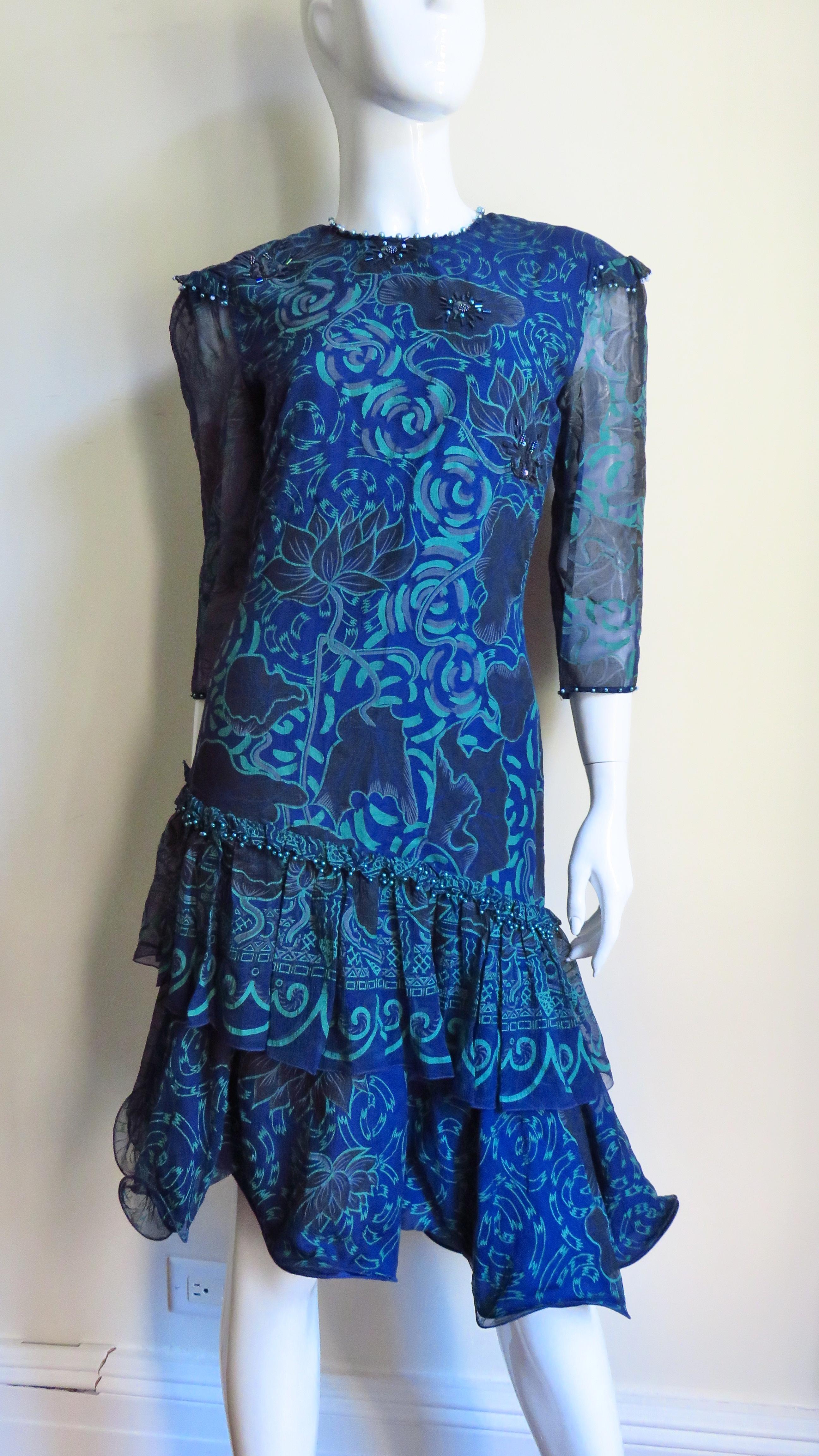 A great silk dress in a beautiful batique print in greens and blues from Zandra Rhodes. It has a crew  neckline, tiny ruffles at the shoulders and 3/4 length sleeves all trimmed in matching blue pearls.  The dress skims the body flaring at the hips