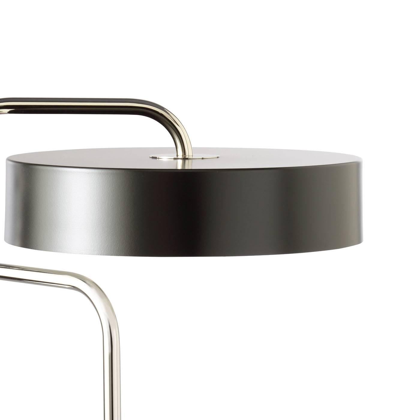 This striking desk lamp is entirely made in metal with a nickel finish and paired with a metal shade painted in a darker tone. This subtle color variation adds elegance to the contemporary silhouette of this piece that features a small round base