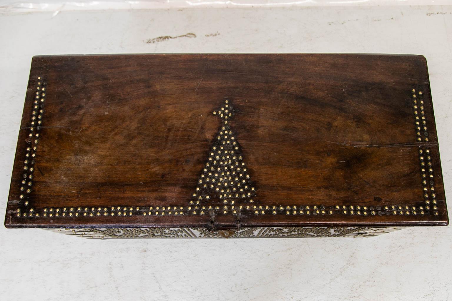 This trunk has brass studwork applied in various decorative patterns. Some of the brass studs are missing. Each front has five applied decorative straps. The tip of one of the right hand straps is missing. The interior hinges have decorative