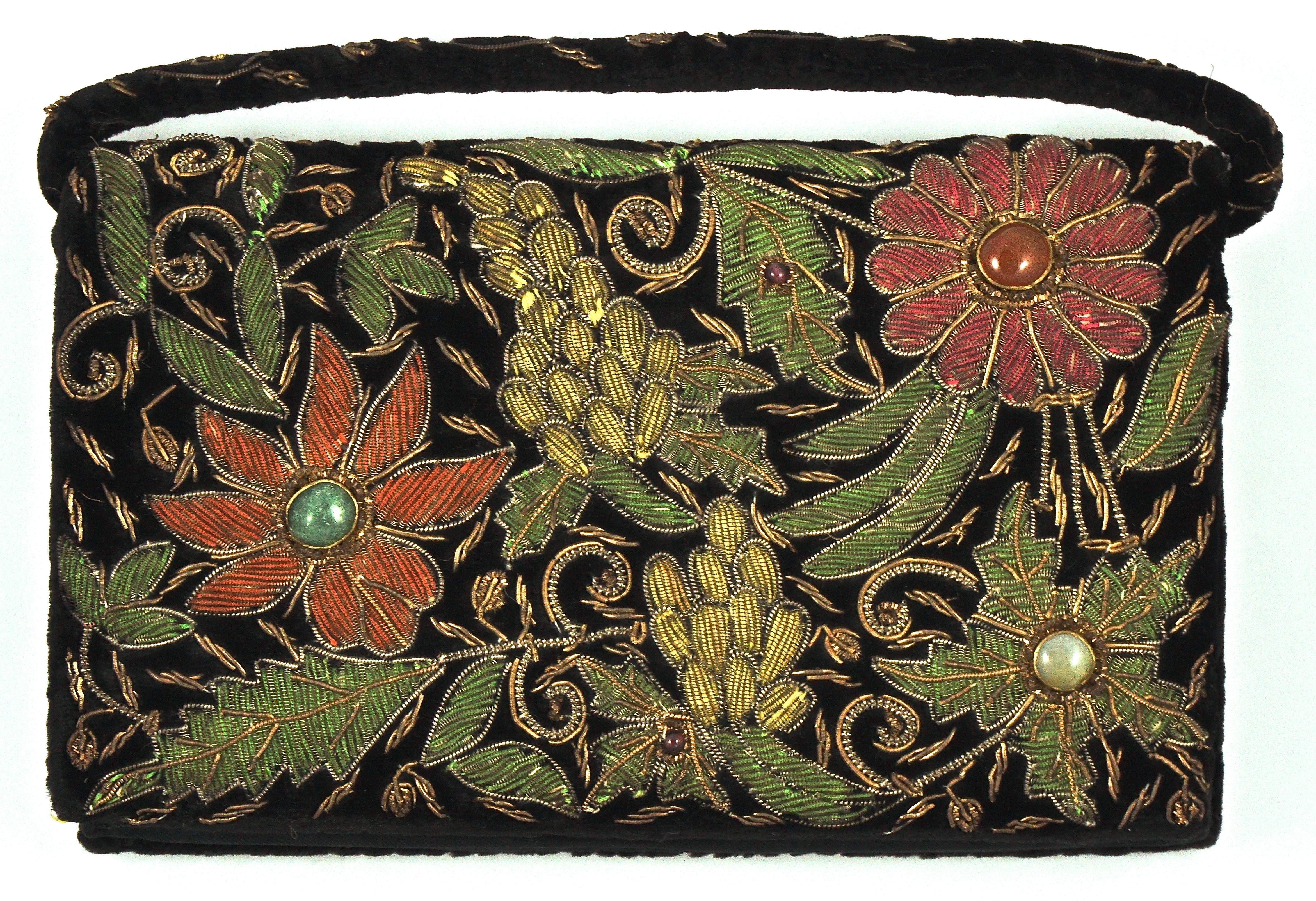 Zardozi floral embroidered black velvet handbag with a snap clasp, featuring golden and silver tone metal work and coloured stone decoration, circa 1950s. The embroidery covers the front and reverse, and the handle is also embroidered. Measuring