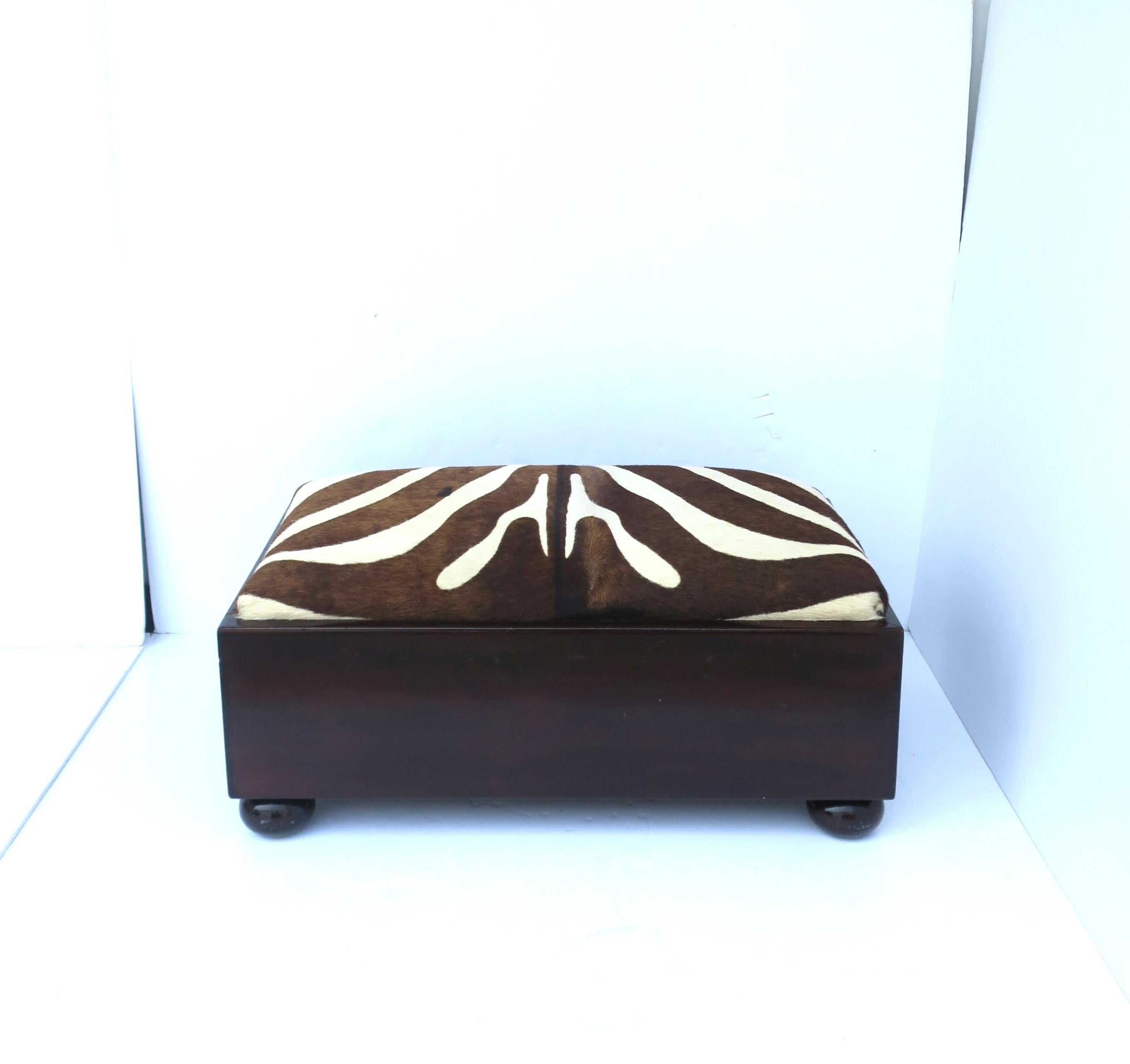 A beautiful wood and zebra hide footstool or low bench / stool, circa early to mid-20th century. Piece is rectangular with bun feet, with a footrest or seat upholstered in authentic zebra hide. 

Dimensions: 15