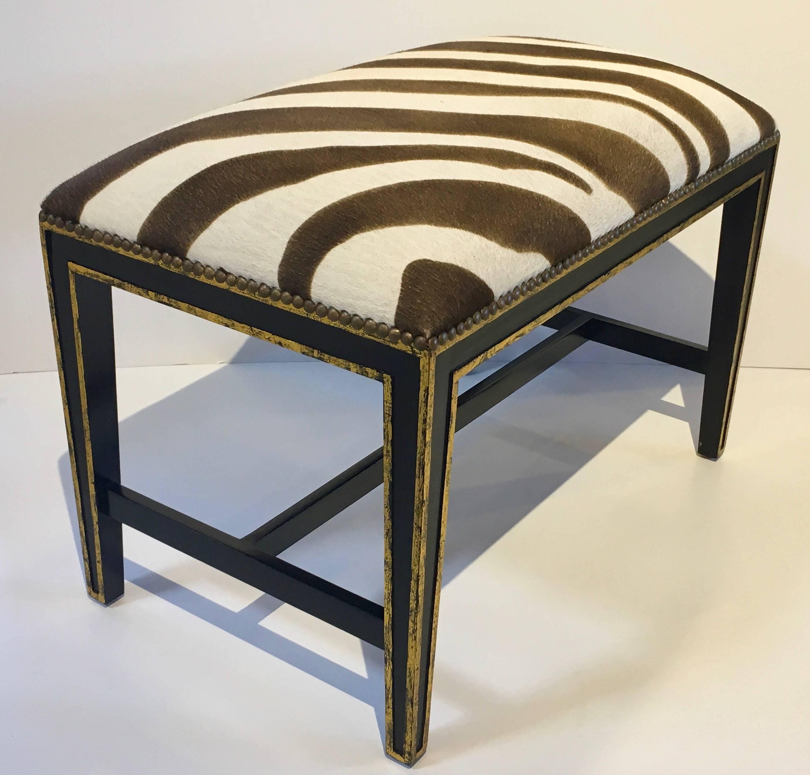 Super pair of zebra hide (pony hair) benches or ottomans with brass nailahead detailing. Sturdy wooden black frames with gilt painted detail and finished with a brass nailhead trim. Size is appropriate for under a console or used as a pair of