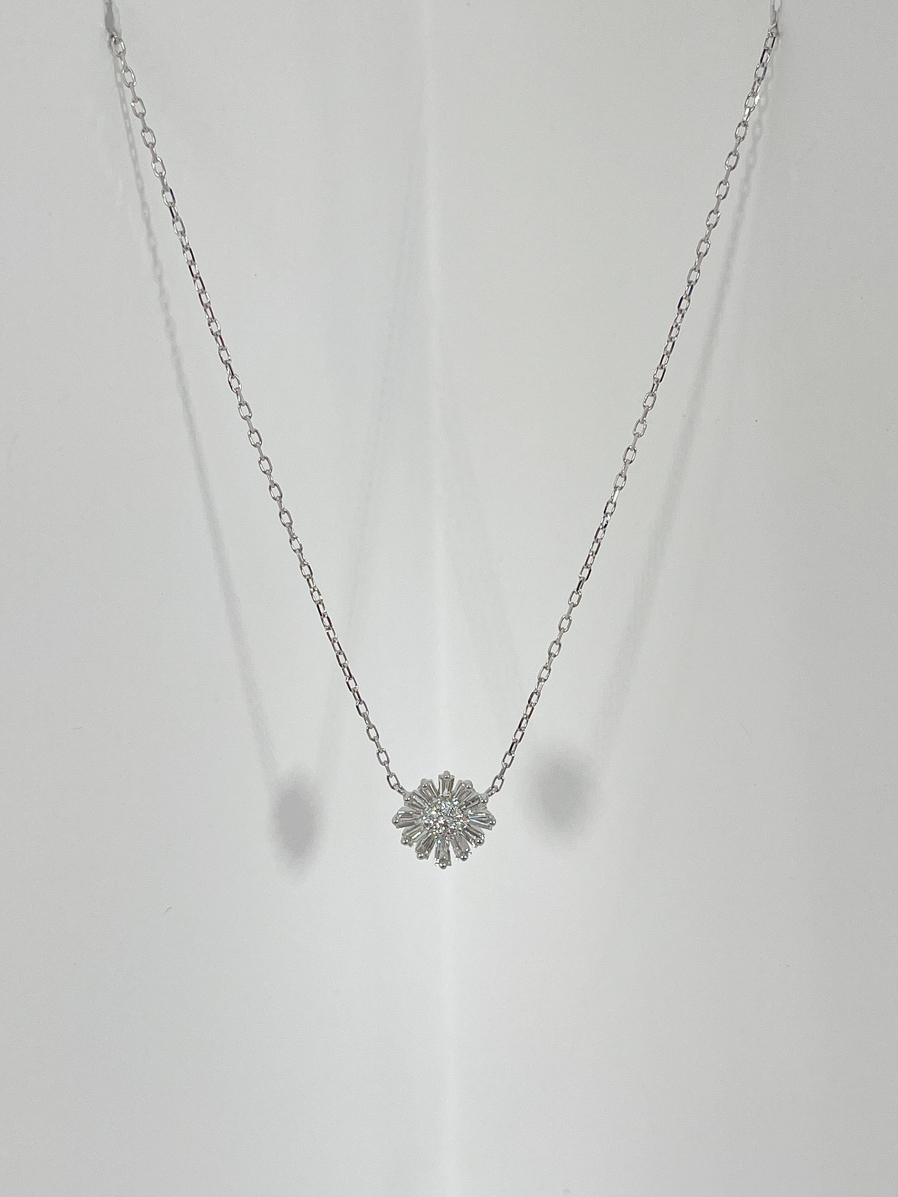 Zeghani 14k white gold .39 CTW diamond flower pendant. The diamonds in the pendant are round and baguette cut, has an O ring clasp to open and close, the length is 18 inches, pendant has a width of 10 mm, and has a total weight of 1.9 grams.