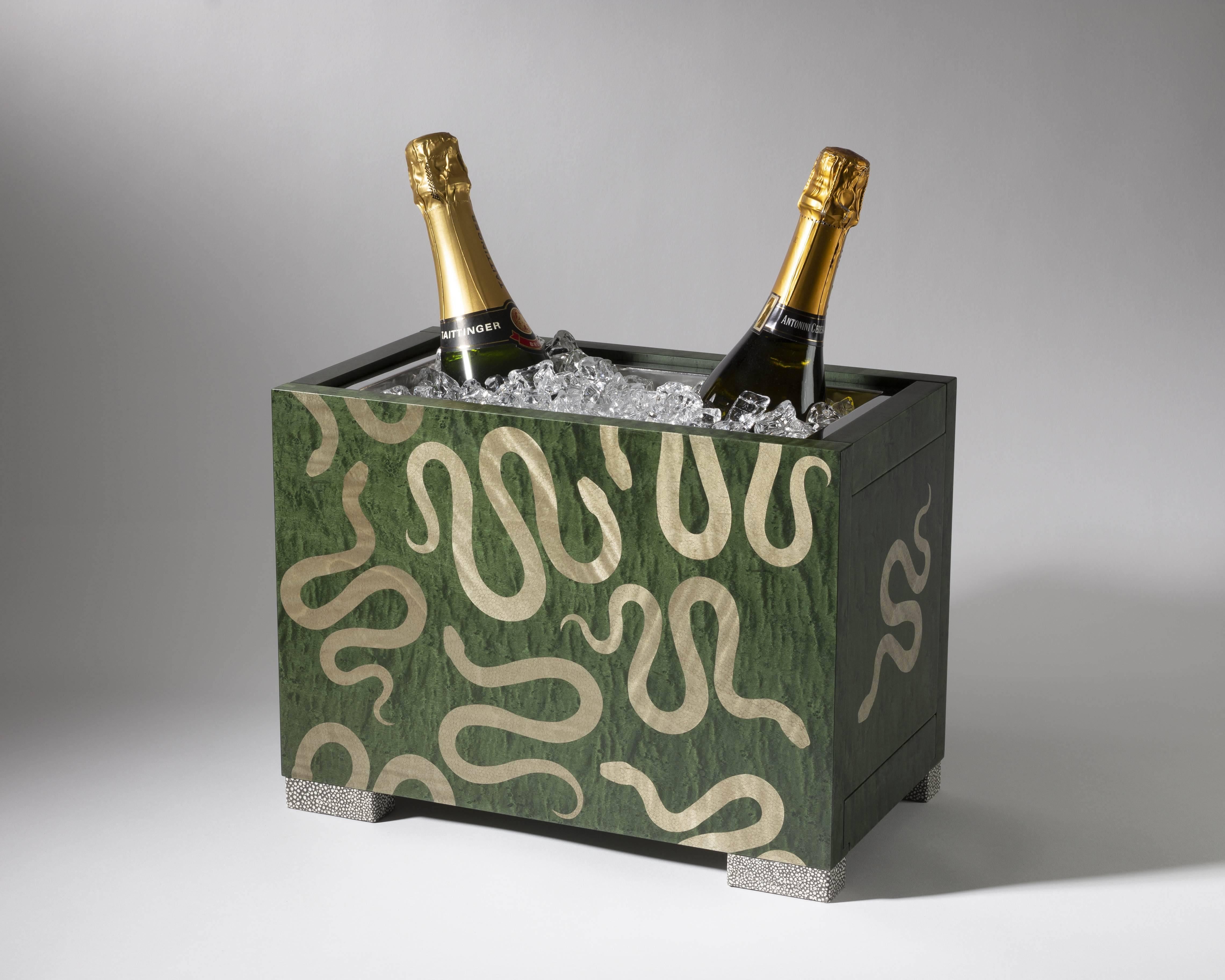Designed as a companion piece to Zelouf & Bell’s Champagne Cart, the Serpent Champagne Cooler in hedge green bird’s-eye maple features a graphic marquetry serpent motif inlaid in figured muted grey-green ripple sycamore.

While seated on ink