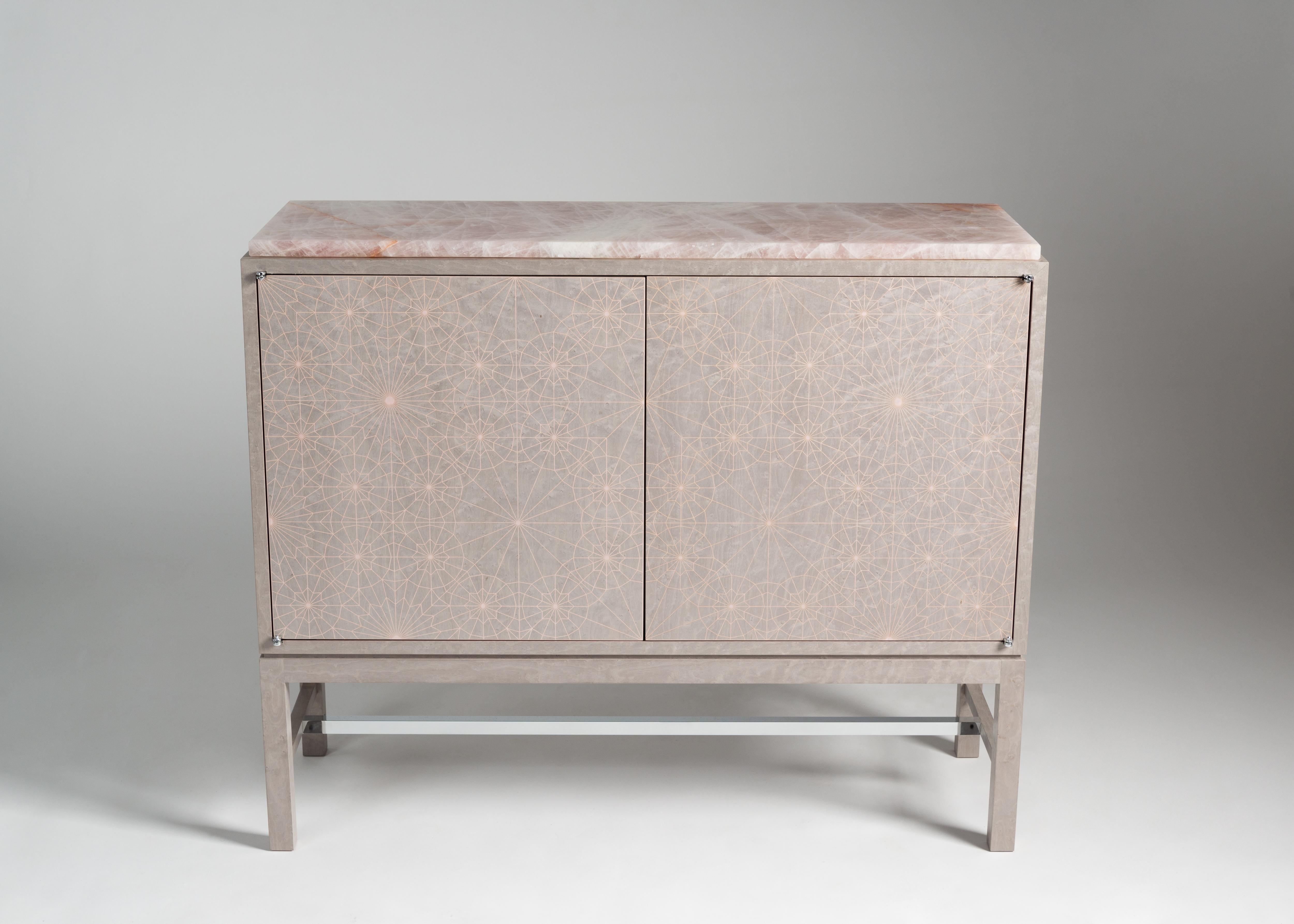 Zelouf & Bell’s two-door constellation cabinet in a dusty pink-infused grey bird’s eye maple features a delicate web of tone-on-tone marquetry in pink ripple sycamore, a secondary top in rose quartz, and a pink ripple sycamore interior with shelves