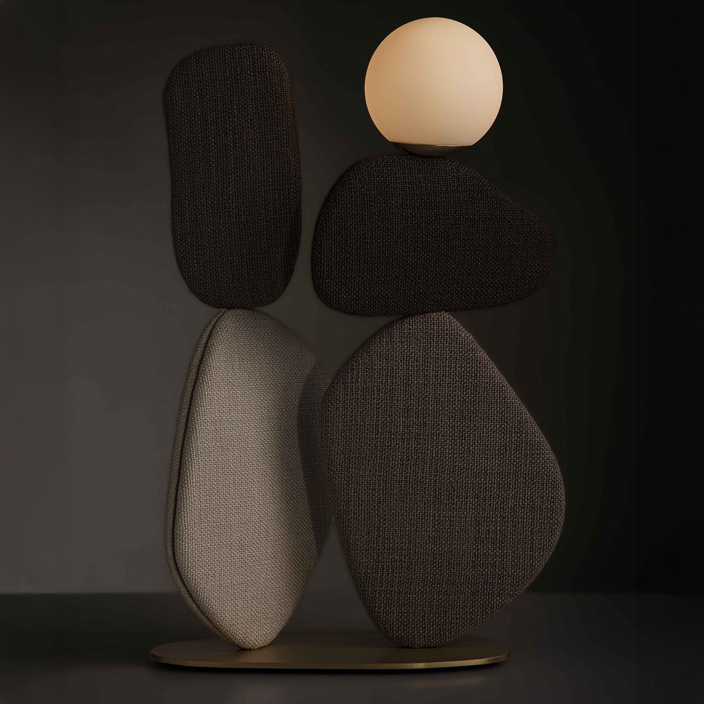 Una lampada da terra scultorea caratterizzata da una base in ottone che sostiene volumi dolcemente curvi in tessuto marrone, ispirati all'arte del bilanciamento della pietra. Questi elementi a forma di petalo possono essere ruotati per creare varie